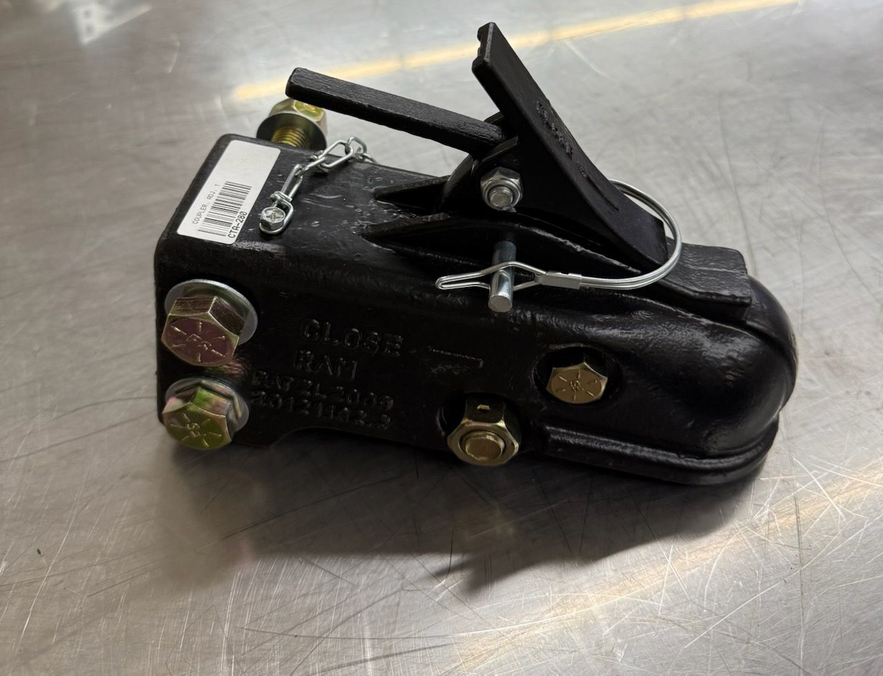 Black trailer coupler with a metal latch, mounted with bolts on a metal surface.