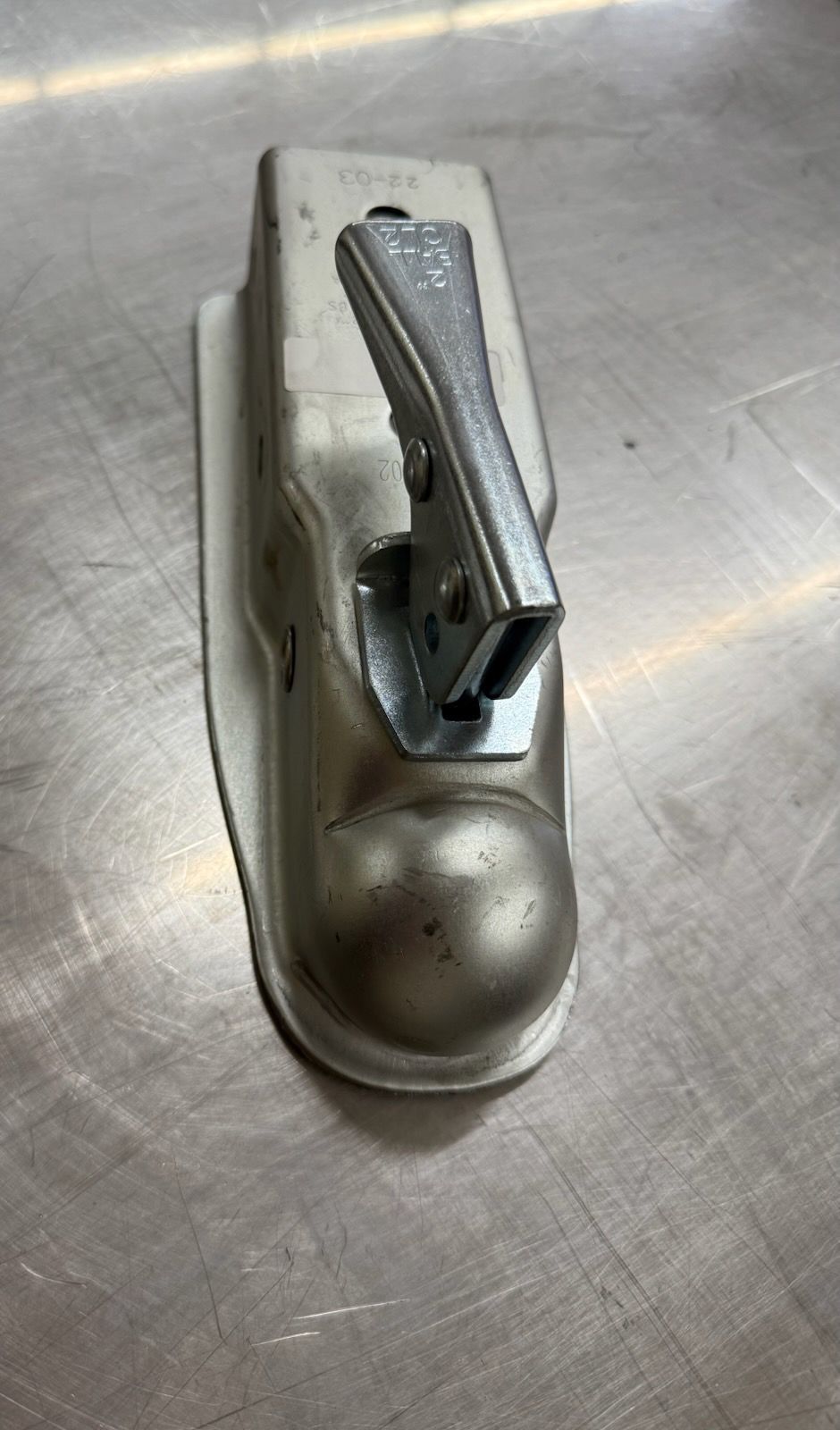 Silver trailer coupler on a metallic surface, with a locking lever.