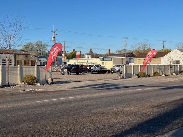 Car lot with parked vehicles, red promotional flags, and a fenced roadside under a clear blue sky