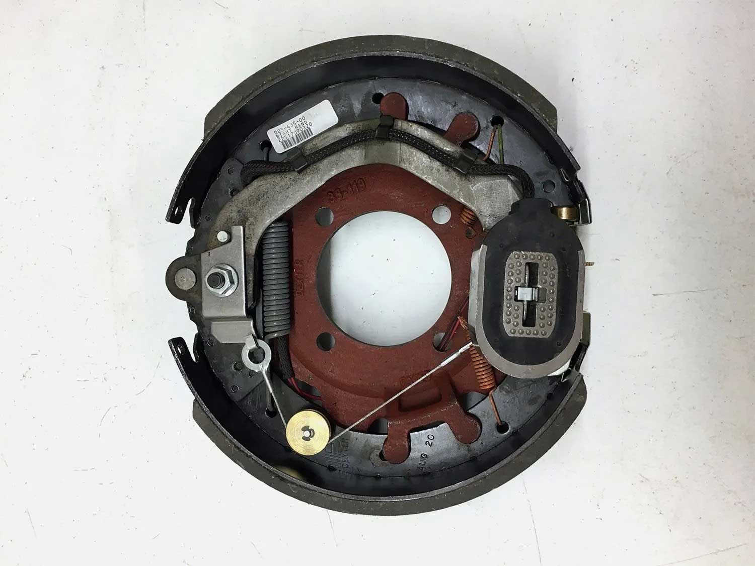 Trailer brake assembly with black brake shoes, a red backing plate, and various springs and hardware.