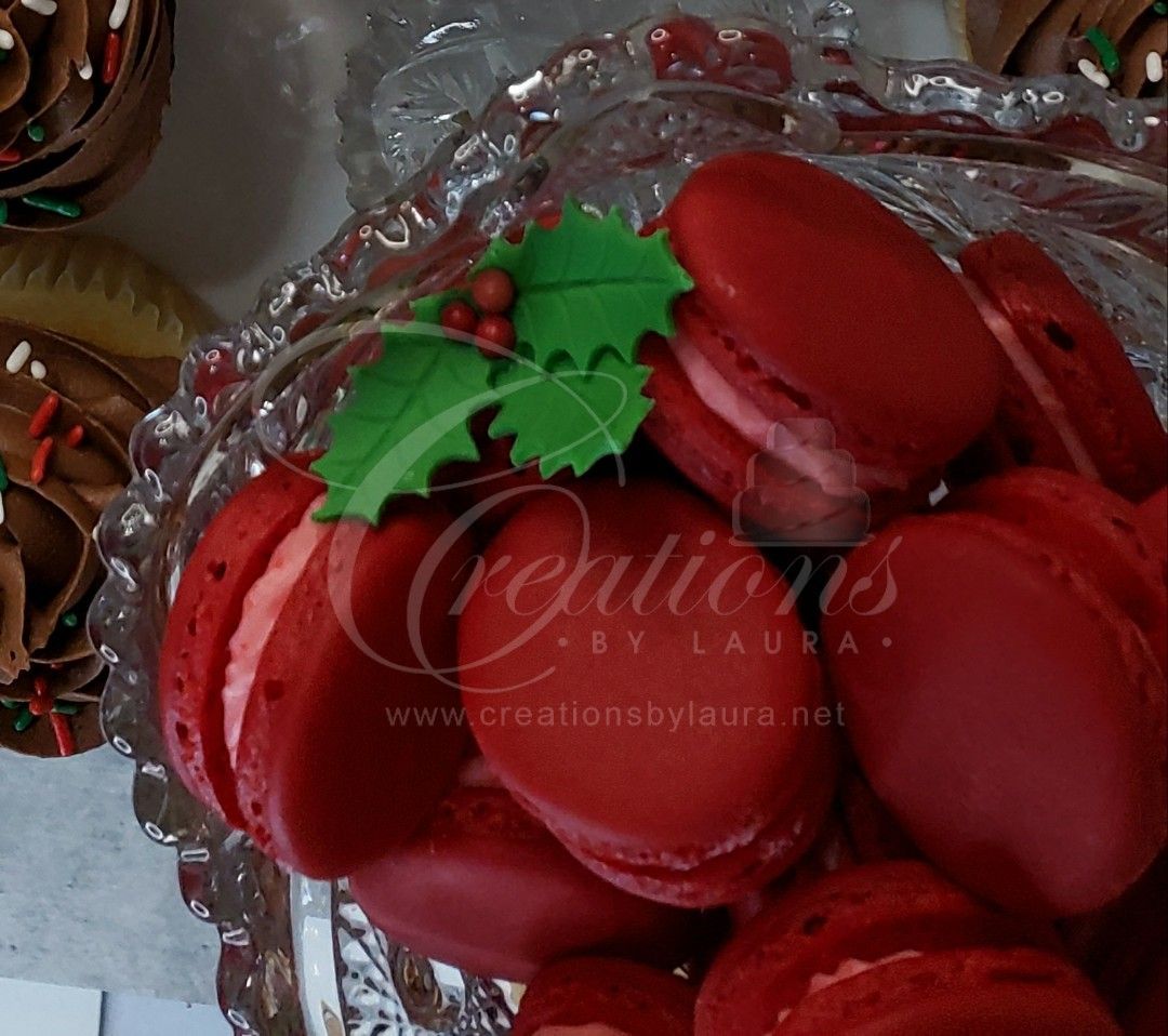 a glass bowl filled with red macarons decorated with green holly leaves