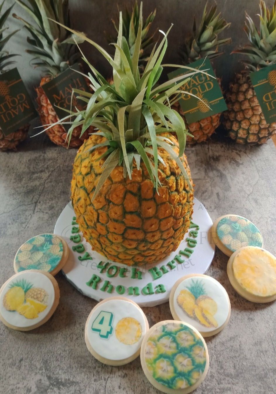 Decorated pineapple centerpiece cake with white frosting cookies around it, arranged on a table with tropical decor