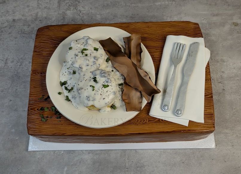 Plate of creamy food on a wooden tray with napkin, plastic fork, and knife design cake