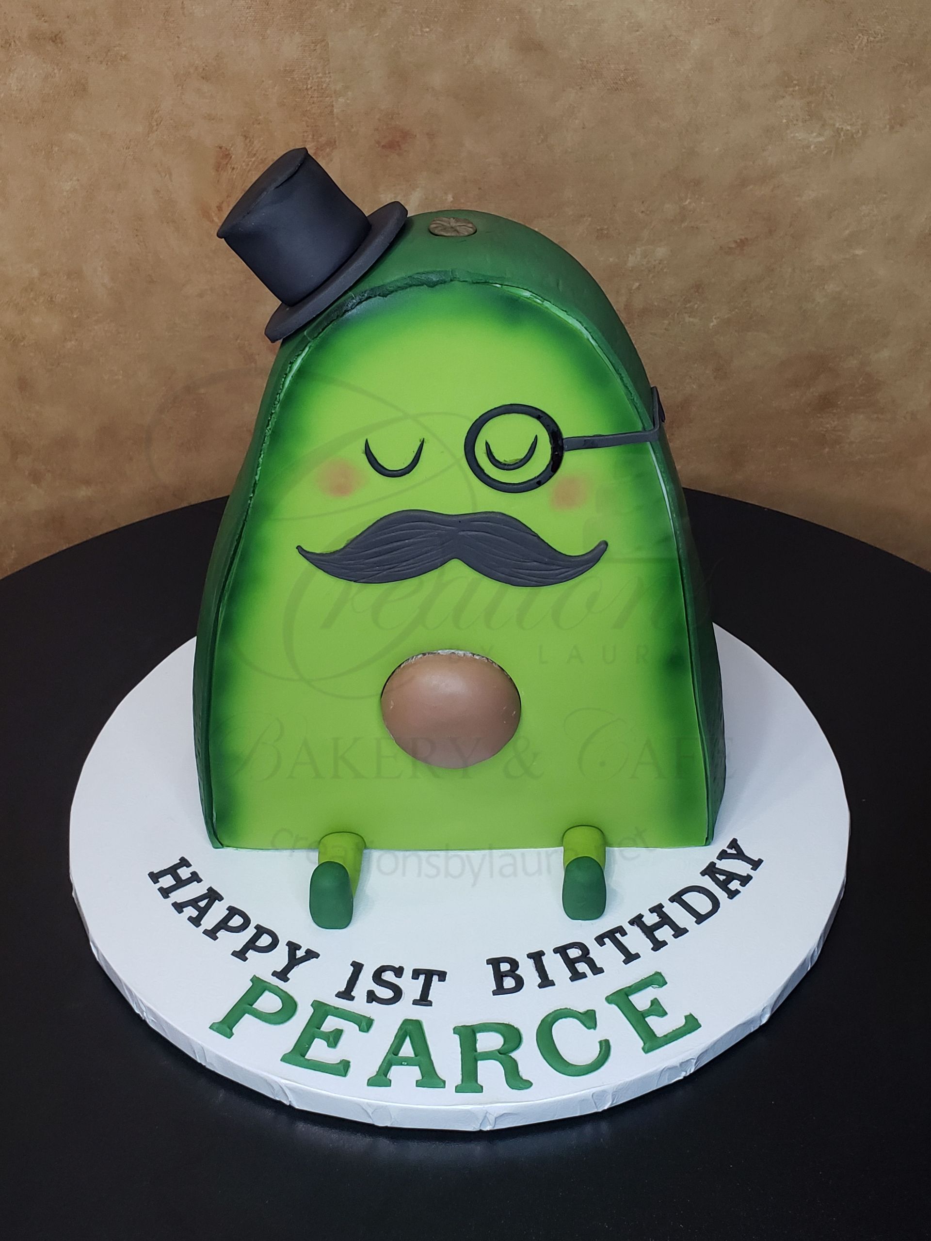 Green cartoon birthday cake with top hat, monocle, mustache, and plaque reading Happy 1st Birthday Pearce