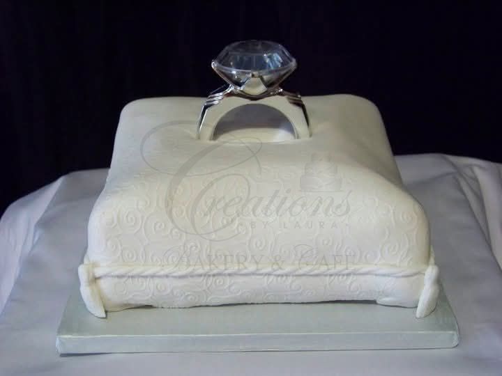 White embroidered cushion with a large diamond ring on top, displayed on a tray against a dark background