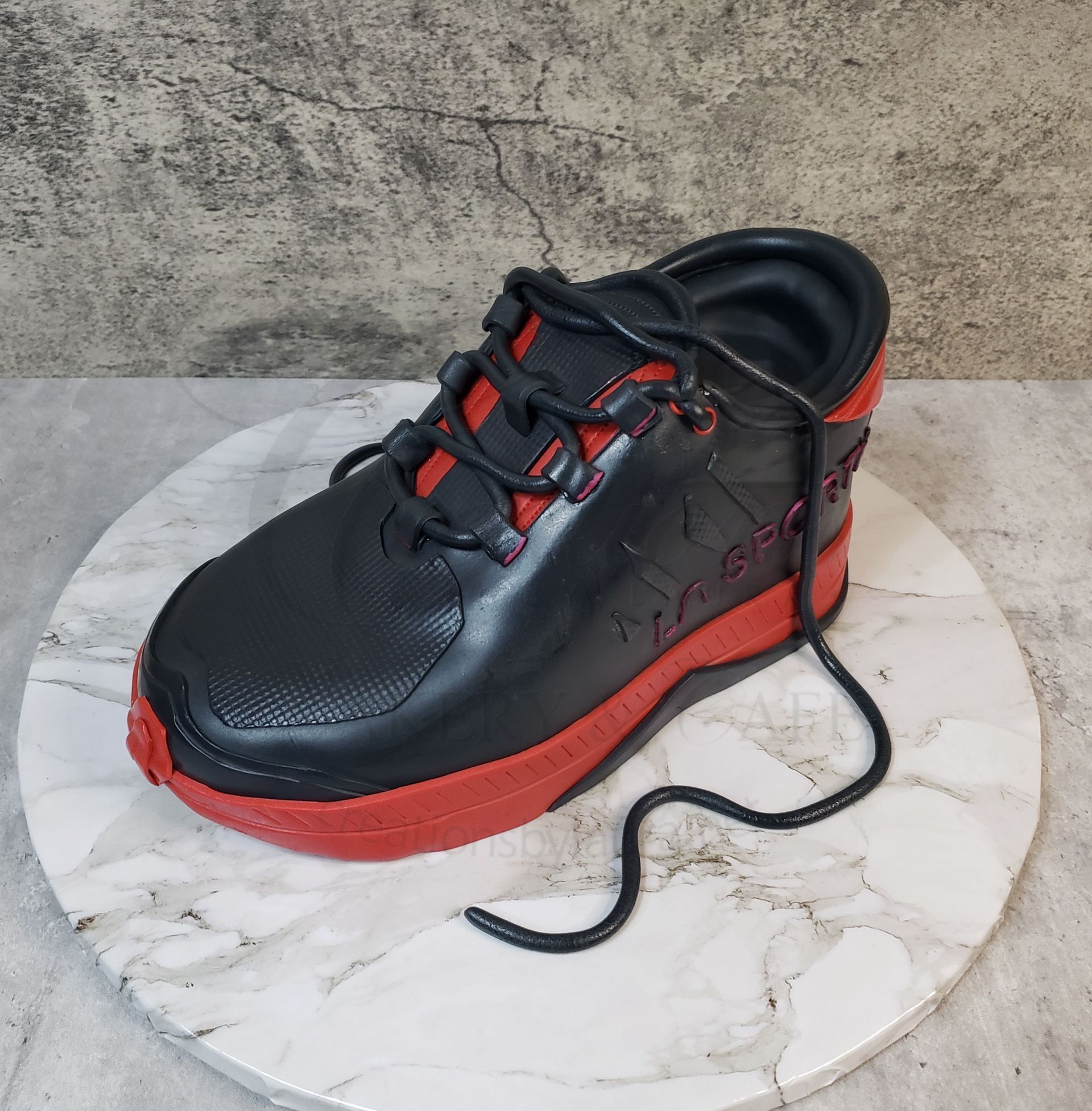 Black and red athletic shoe with loose laces on a marble surface against a textured wall