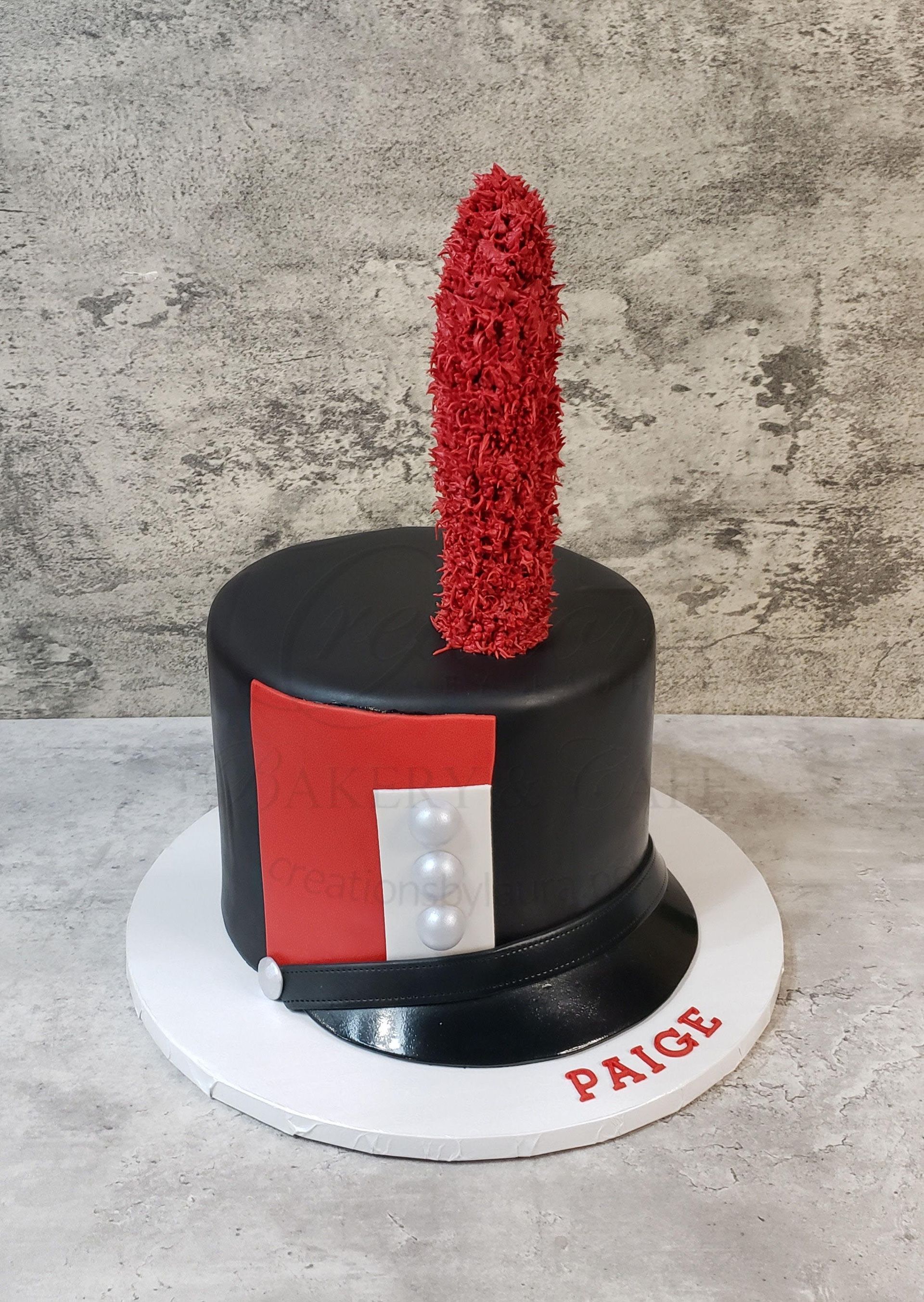 Black cake with red-and-white details and a red topper on a white board labeled PAIGE