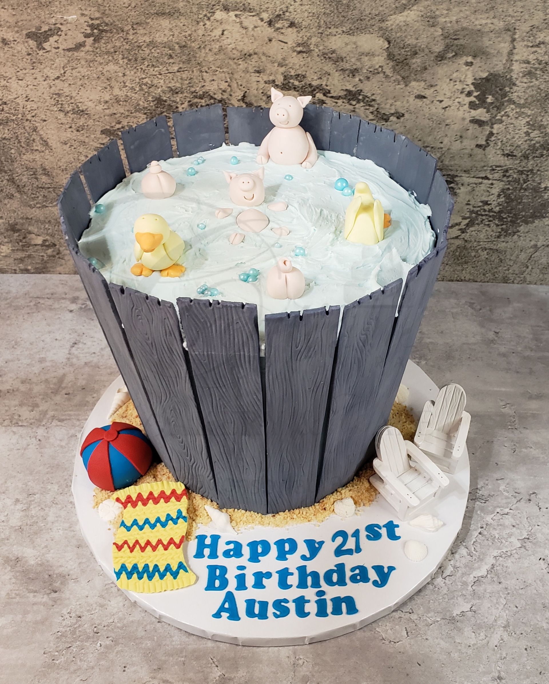 Blue animal-themed birthday cake with Happy 21st Birthday Austin and beach toys on a white base
