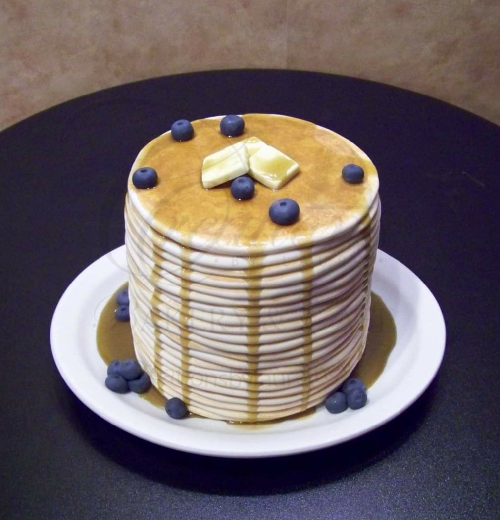 Stack of pancakes topped with blueberries and butter on a white plate