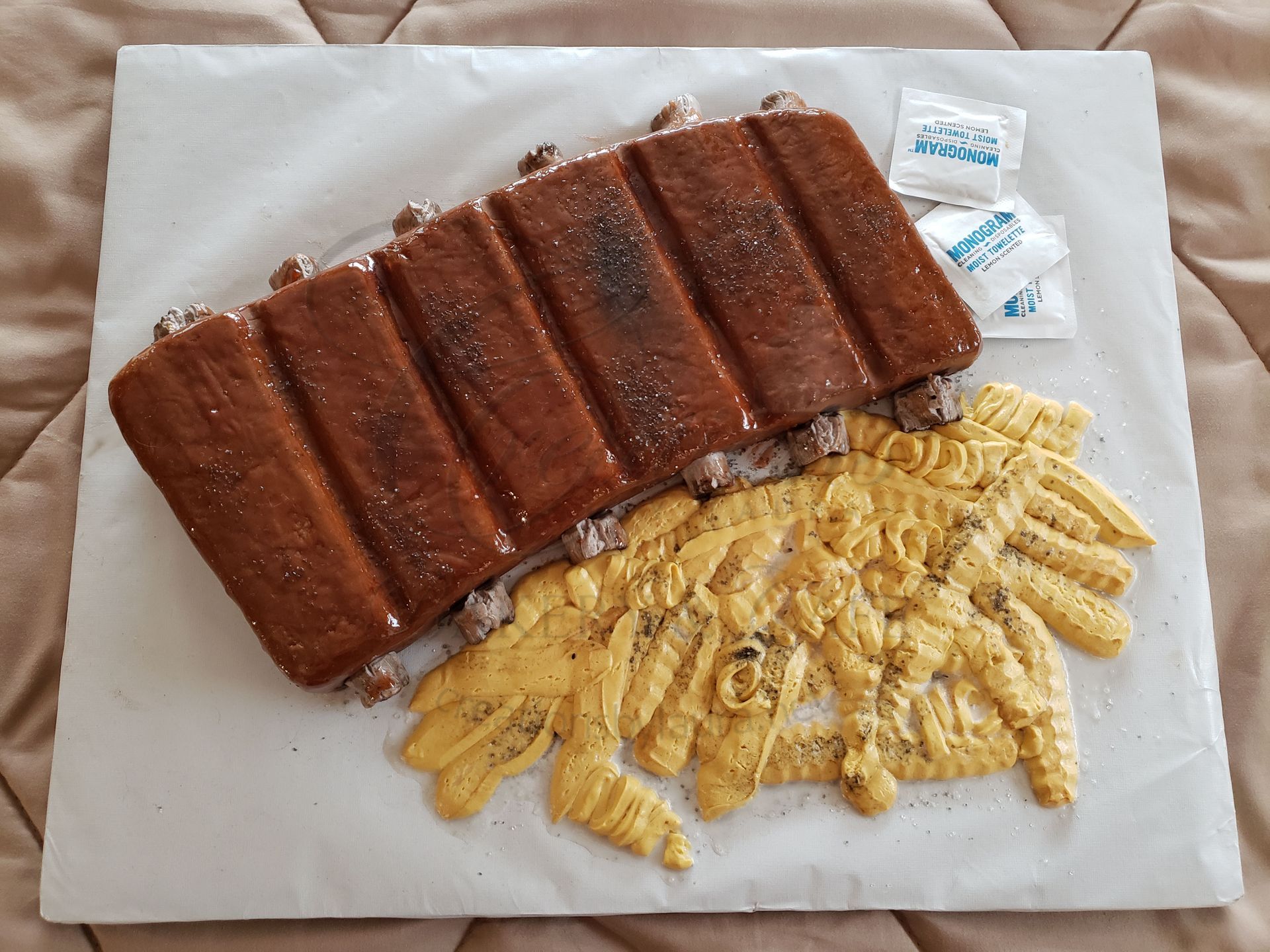 Barbecue ribs with crinkle-cut fries on a white plate, with small condiment packets nearby
