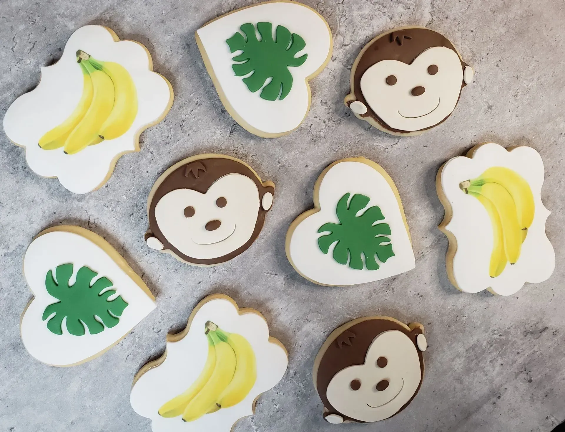 A collection of jungle-themed cookies shaped like monkeys, green tropical leaves, and bunches of yellow bananas.