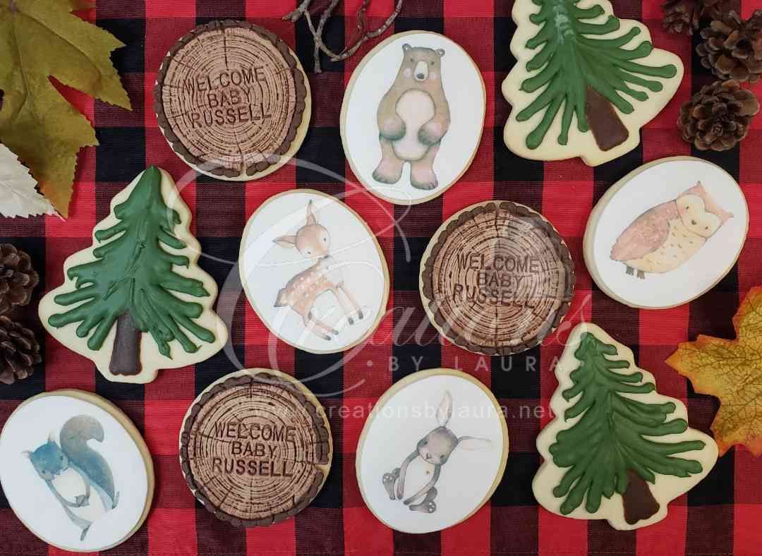 A collection of decorated woodland-themed cookies, including forest animals, trees, and wood-grain discs, on a plaid cloth.