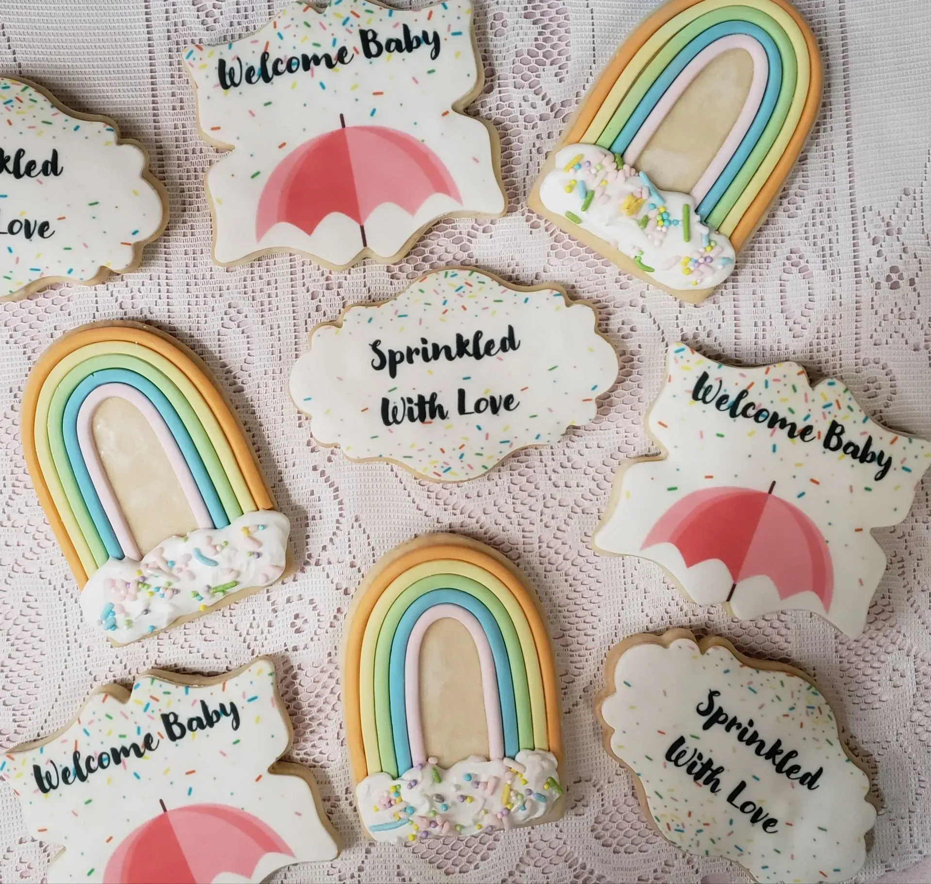 Custom cookies decorated with pastel rainbows and umbrellas with the text Welcome Baby and Sprinkled With Love.