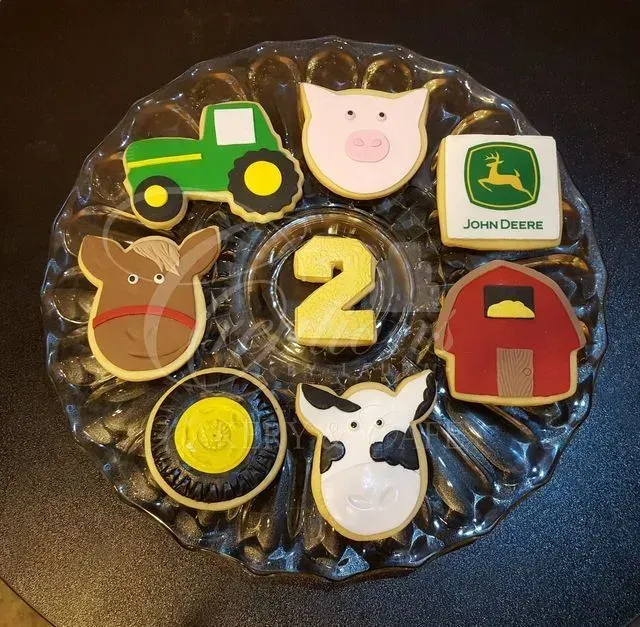 Farm-themed decorated number 2 cookie with tractor, animals, barn, and John Deere logo on a glass plate