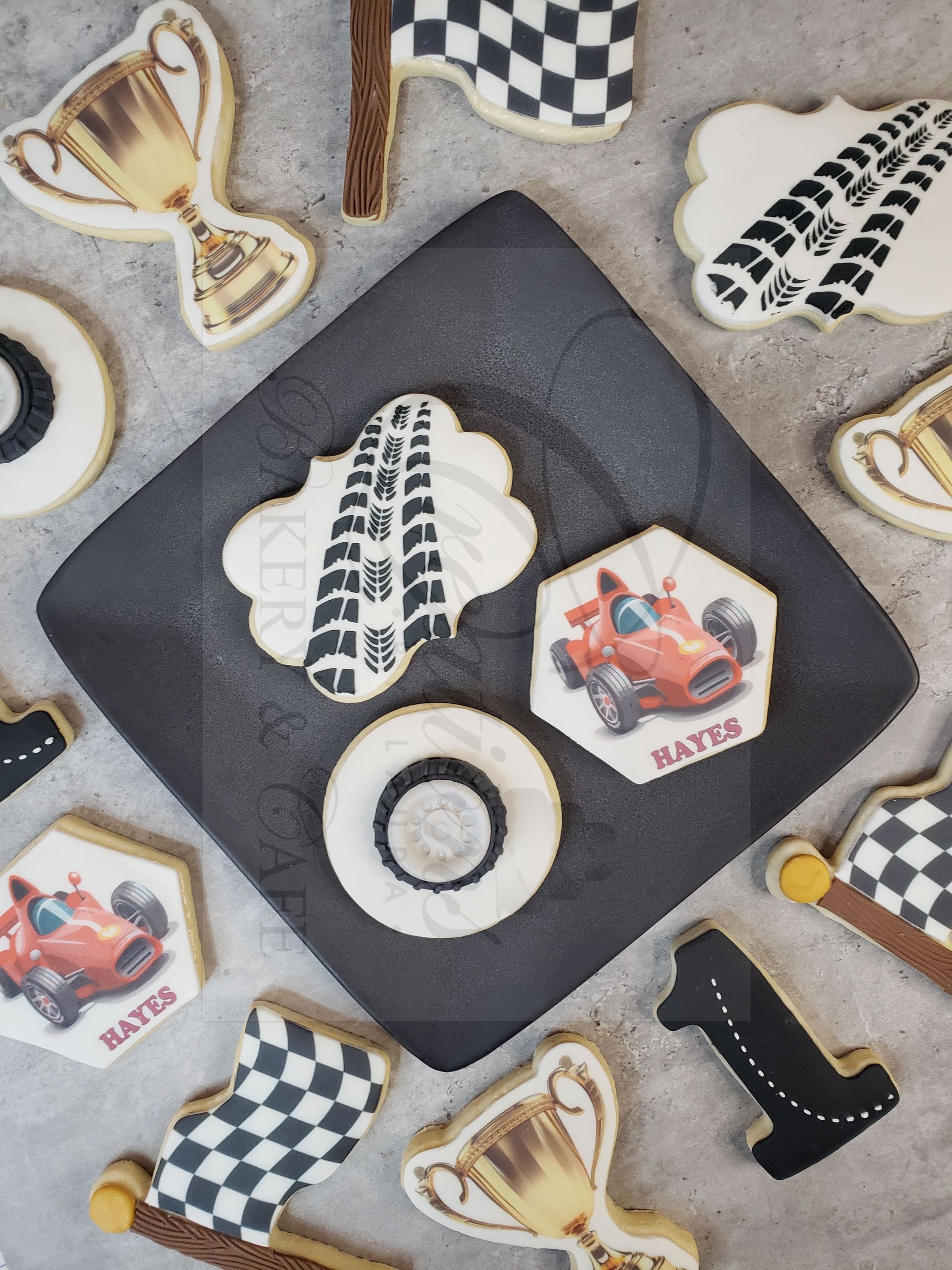 Race car-themed cookies on a gray surface, with checkered flags, trophy, tire tracks, and black-and-white details