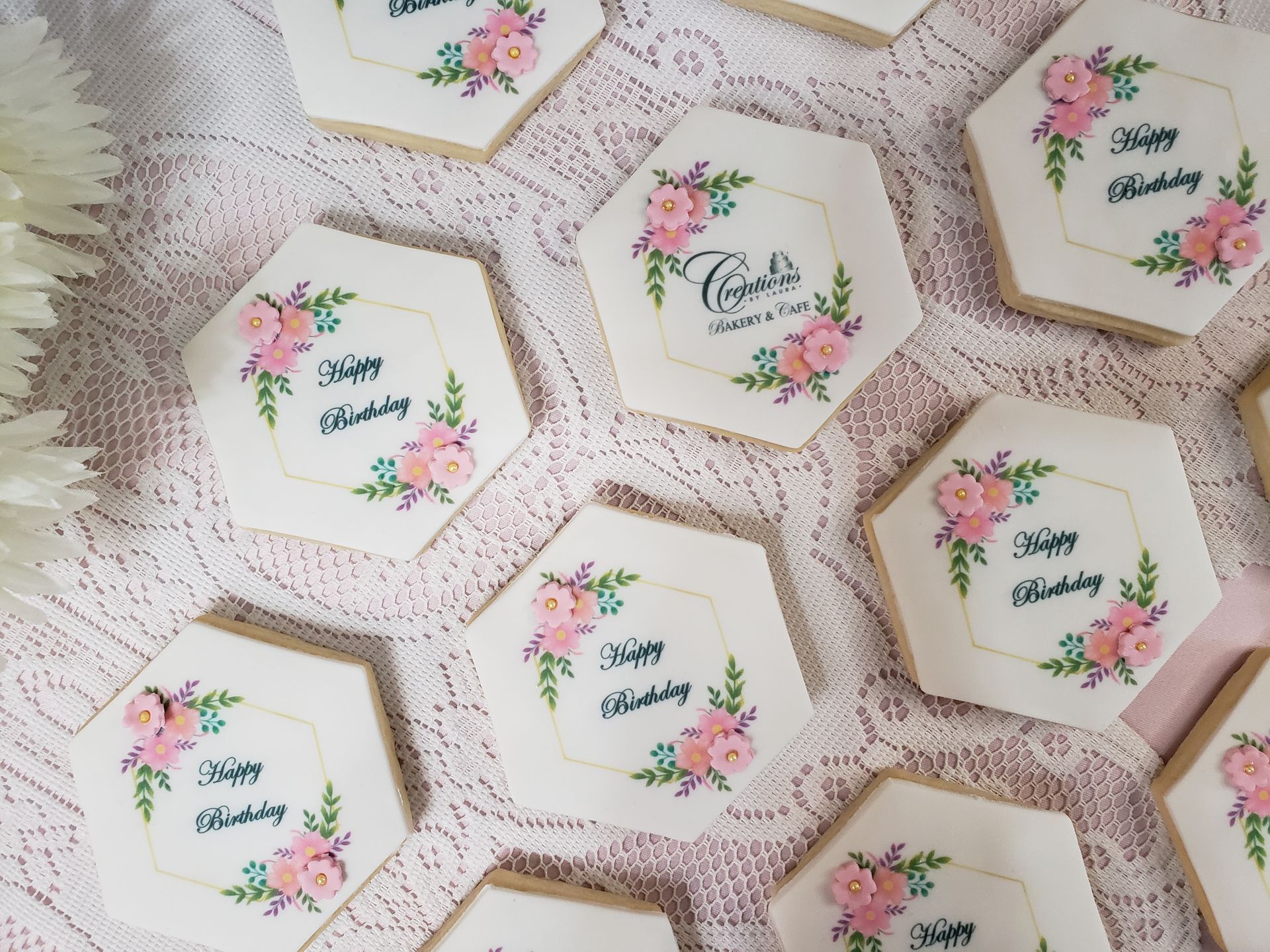 Assorted octagonal floral cookies with pastel pink flowers and green leaves on a lace tablecloth