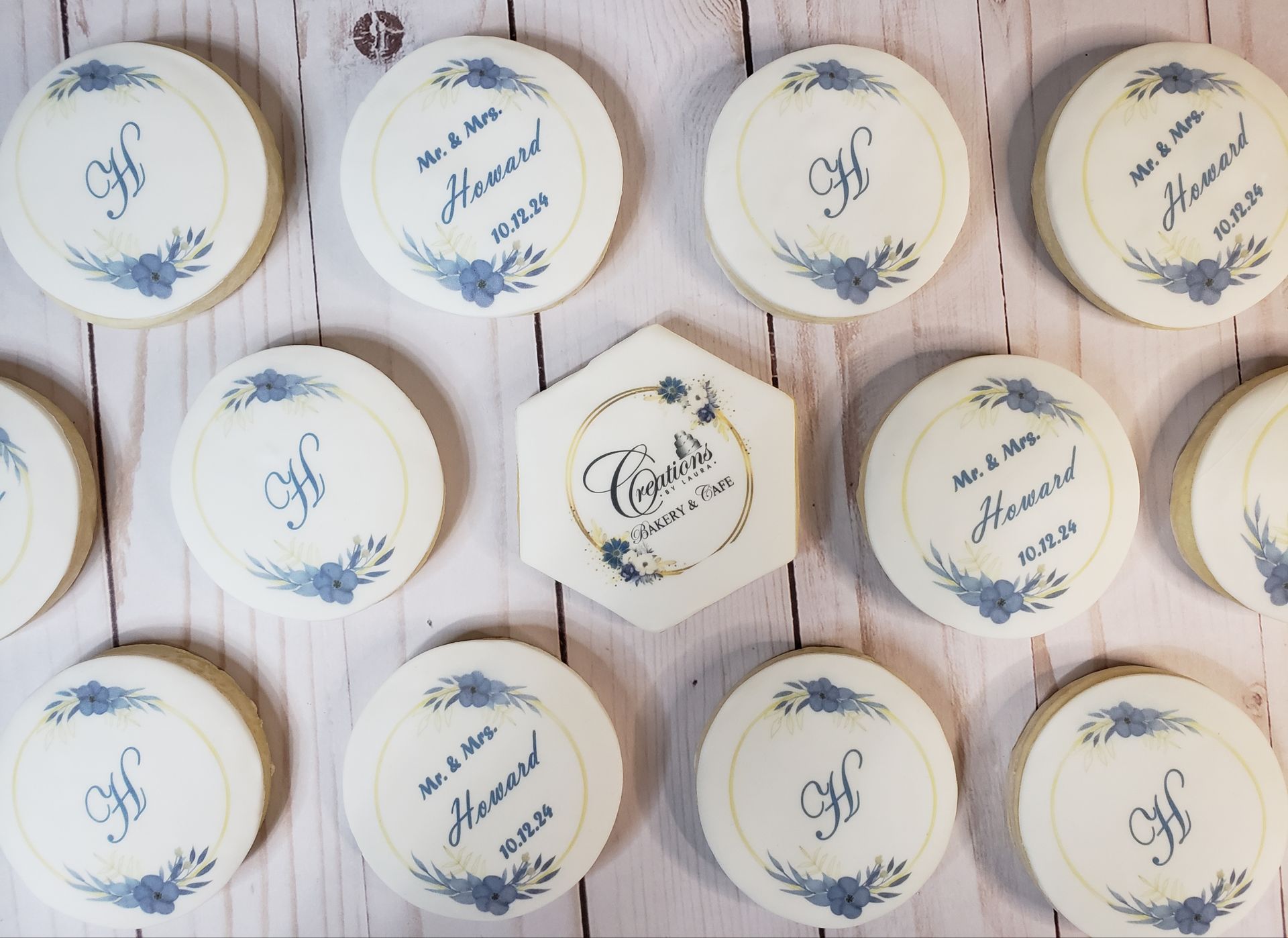 White round favor cookies with blue monograms and script, arranged on a rustic wooden surface.