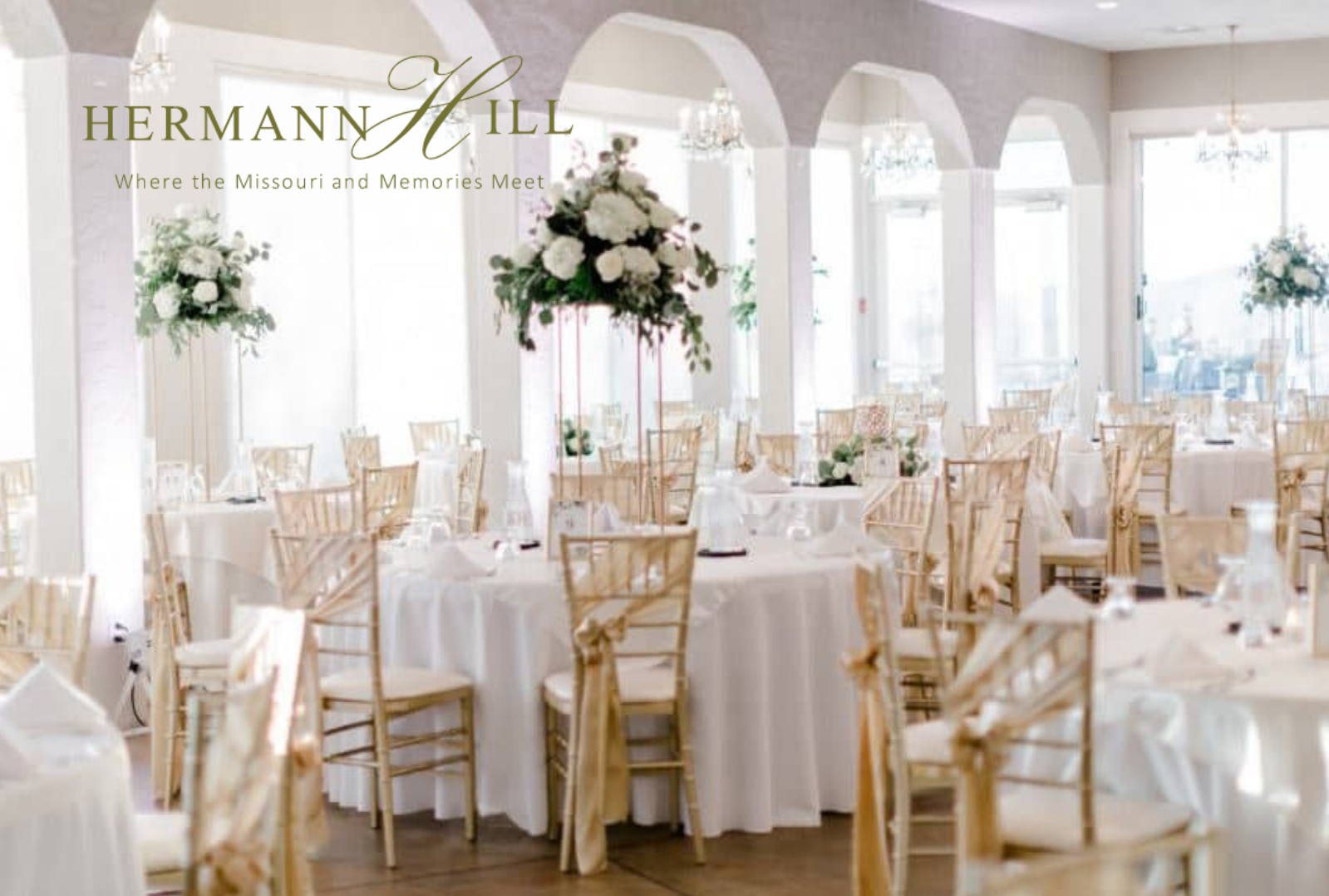 Elegant wedding reception venue with white round tables, gold chairs, and tall floral centerpieces