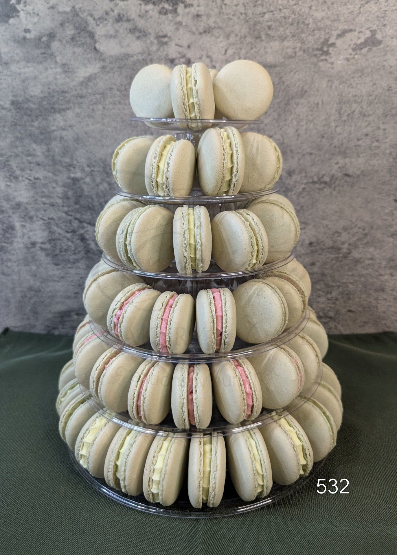 A tiered stand holding a pyramid of off-white macarons with light-colored fillings against a textured gray background.