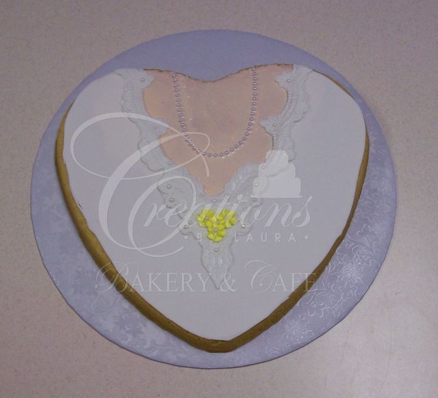 Heart-shaped cake with white icing, lace details, a pearl-style necklace, and yellow floral accents on a light blue base.