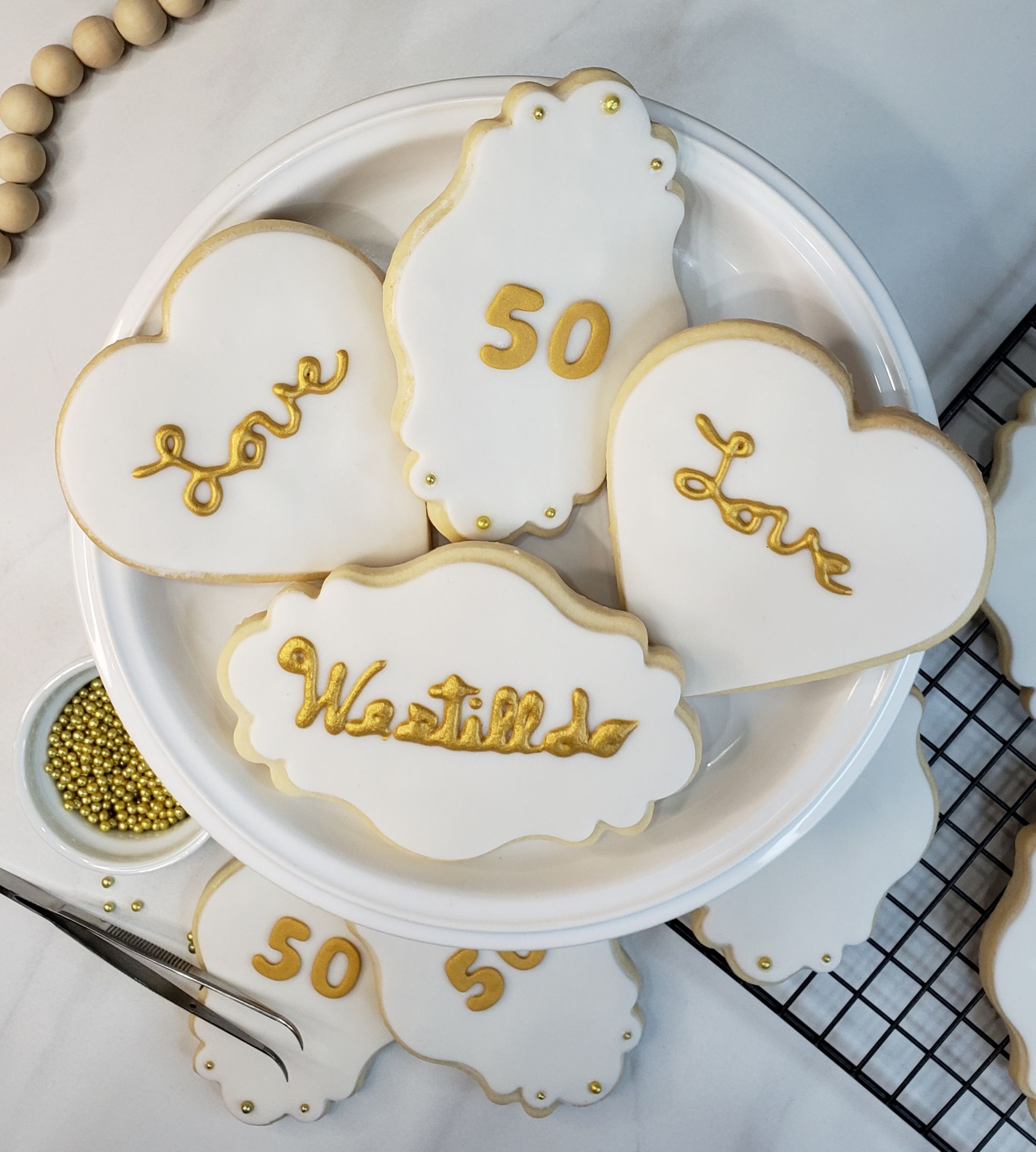 White and gold cookies for a 50th anniversary on a plate, featuring heart shapes and 