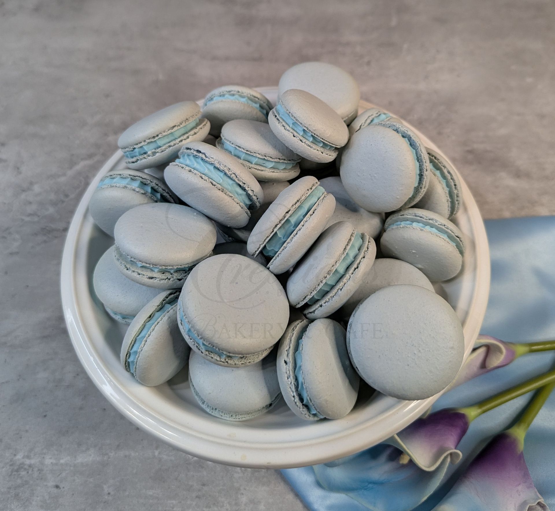 White bowl filled with pale blue and white macarons on a gray surface