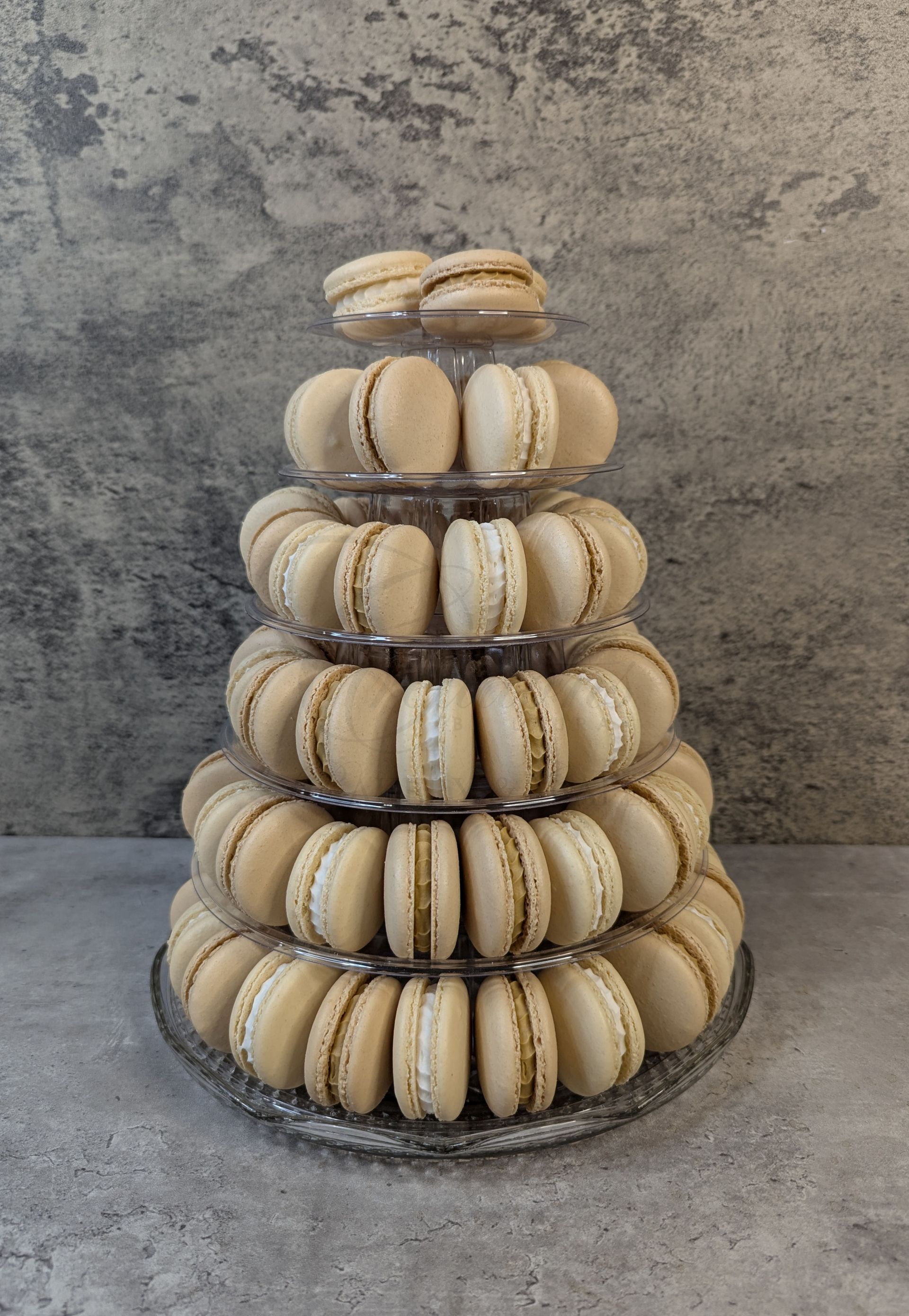 Tiered display of beige macarons on a metal stand against a gray textured wall
