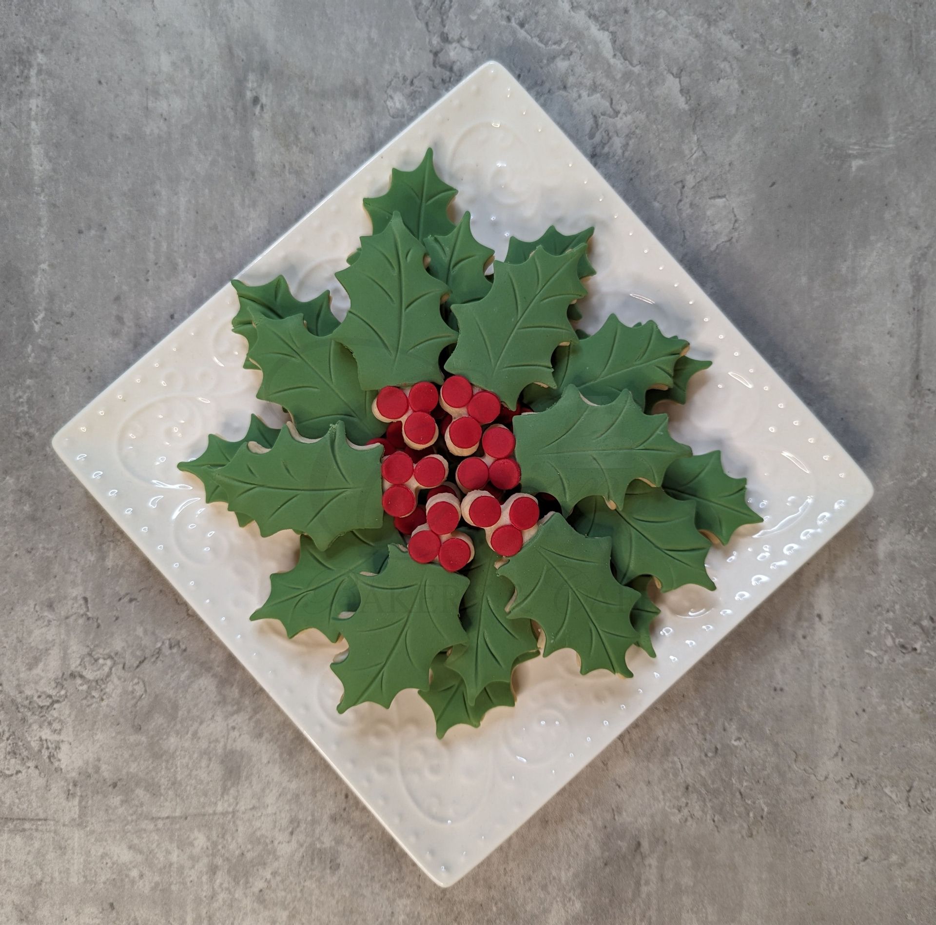 Decorative white plate with green holly leaves and red berries on a gray surface