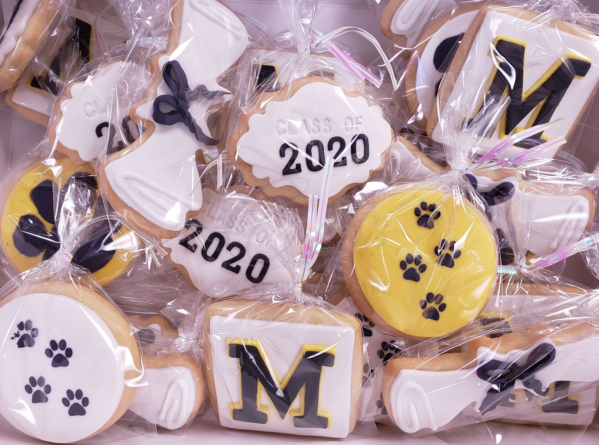 Assorted decorated cookies with paw prints, butterflies, and “2020” and “M” designs in clear packaging