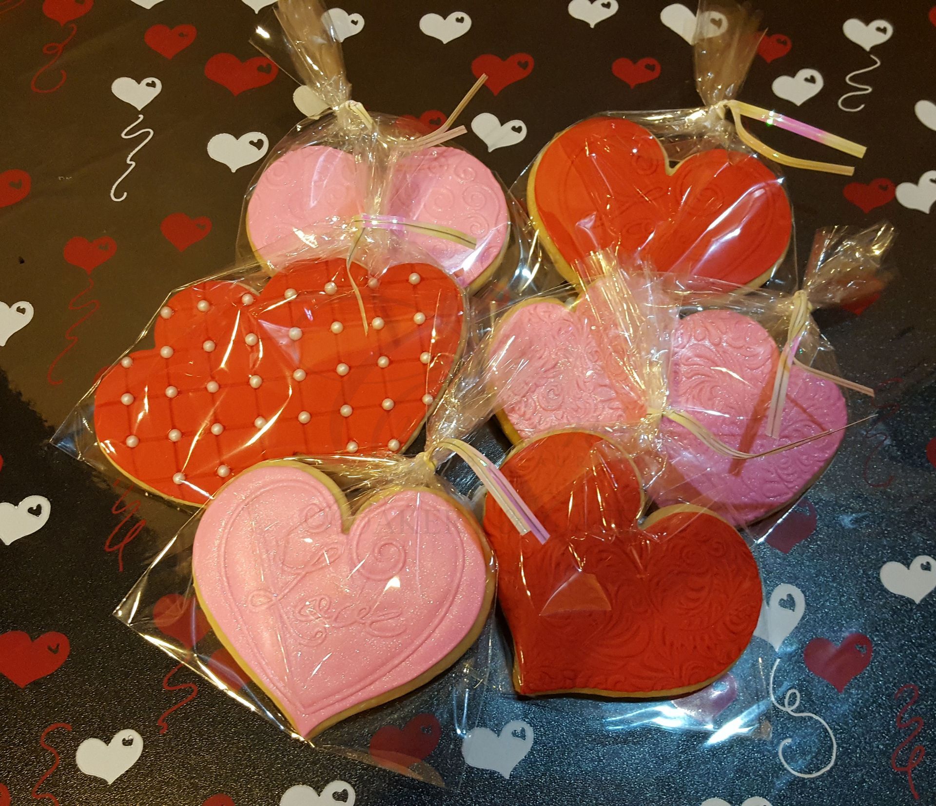 Heart-shaped lollipops in red, pink, and polka-dot designs wrapped in clear plastic on a dark background.