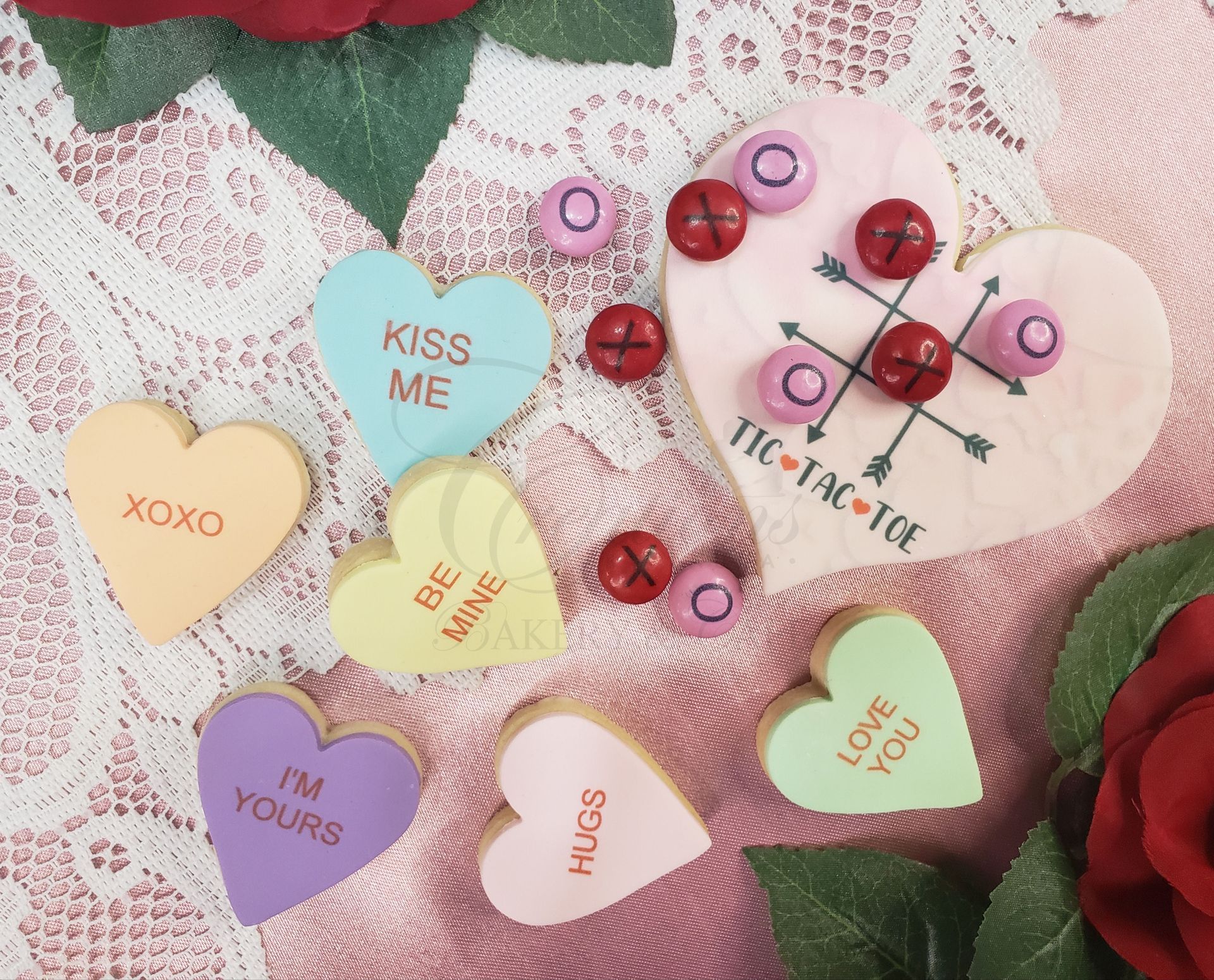 Valentine-themed paper hearts and red bead pins arranged on pink fabric and green leaves