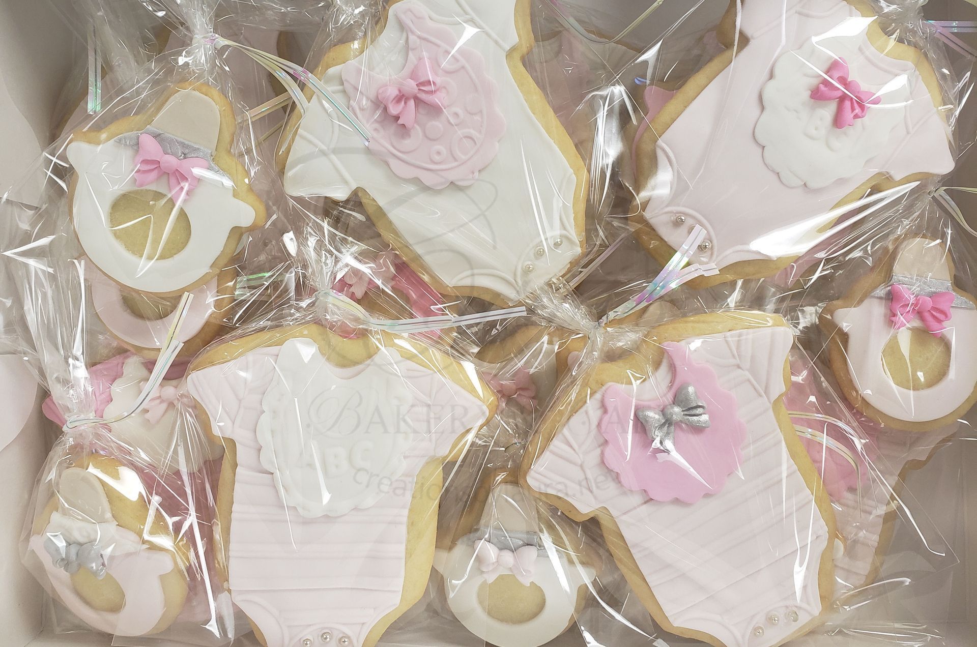 Assorted pink and white decorated cookies wrapped in clear plastic bags, arranged together.