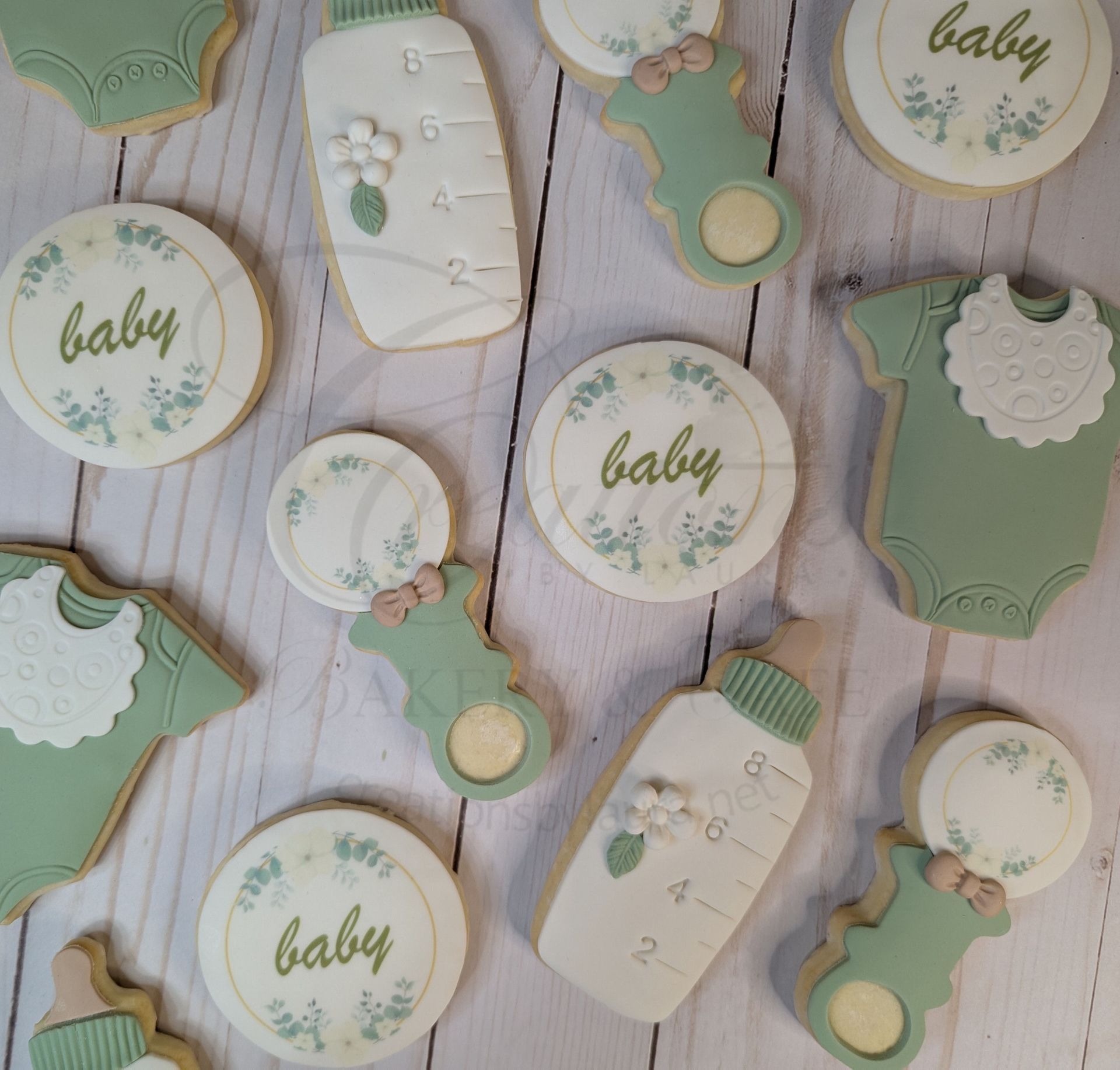 Mint and cream baby shower cookies with baby text and small floral decorations on a wooden surface
