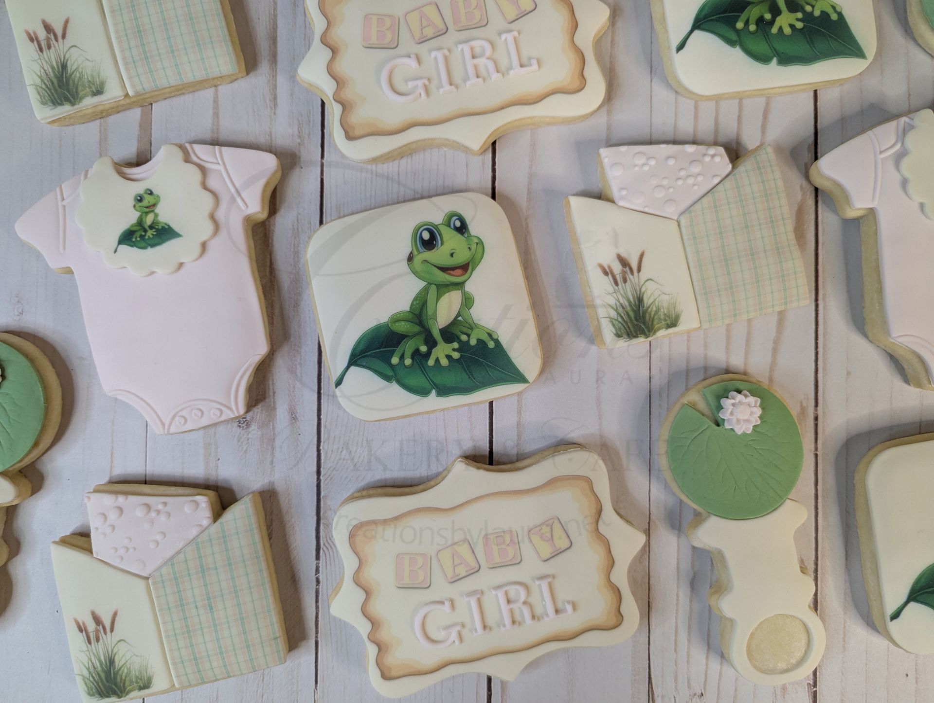 Frosted baby shower cookies with green frogs, onesies, bibs, and boy-girl designs on a white surface