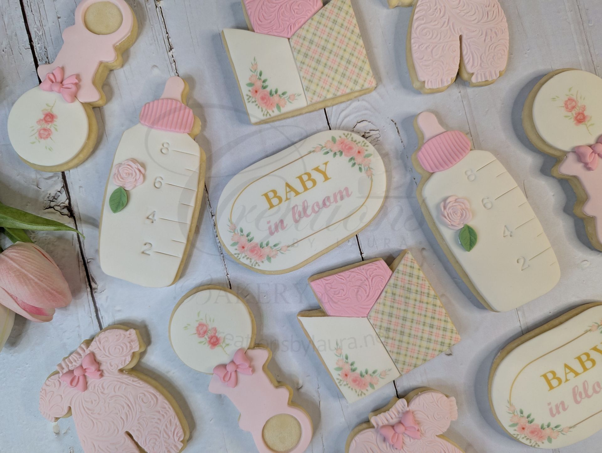 Pastel baby shower paper cutouts on a gray polka-dot background, including bottles, rattle, bibs, and banners