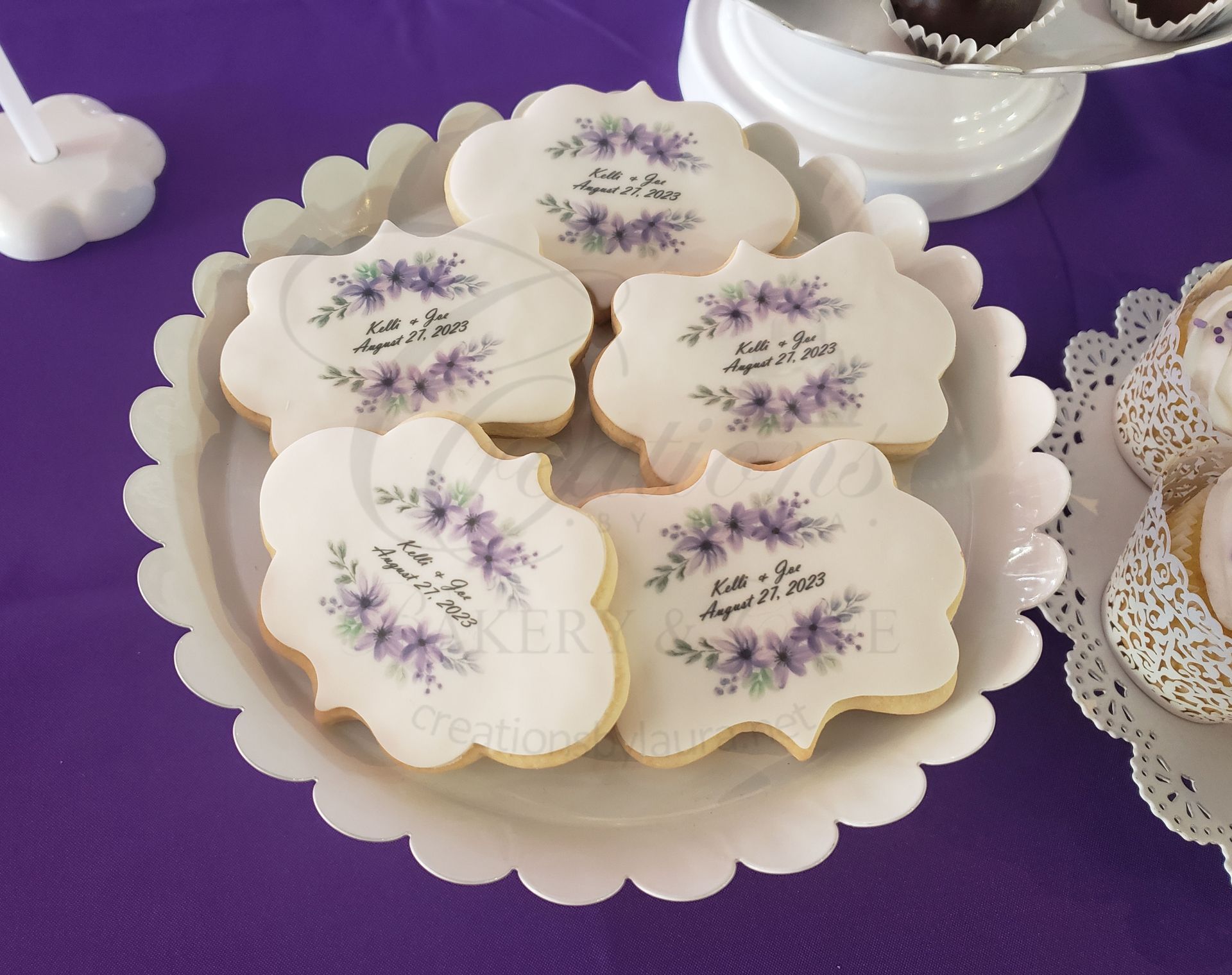 Lavender-frosted flower cookies on a scalloped gold tray against a purple tablecloth.