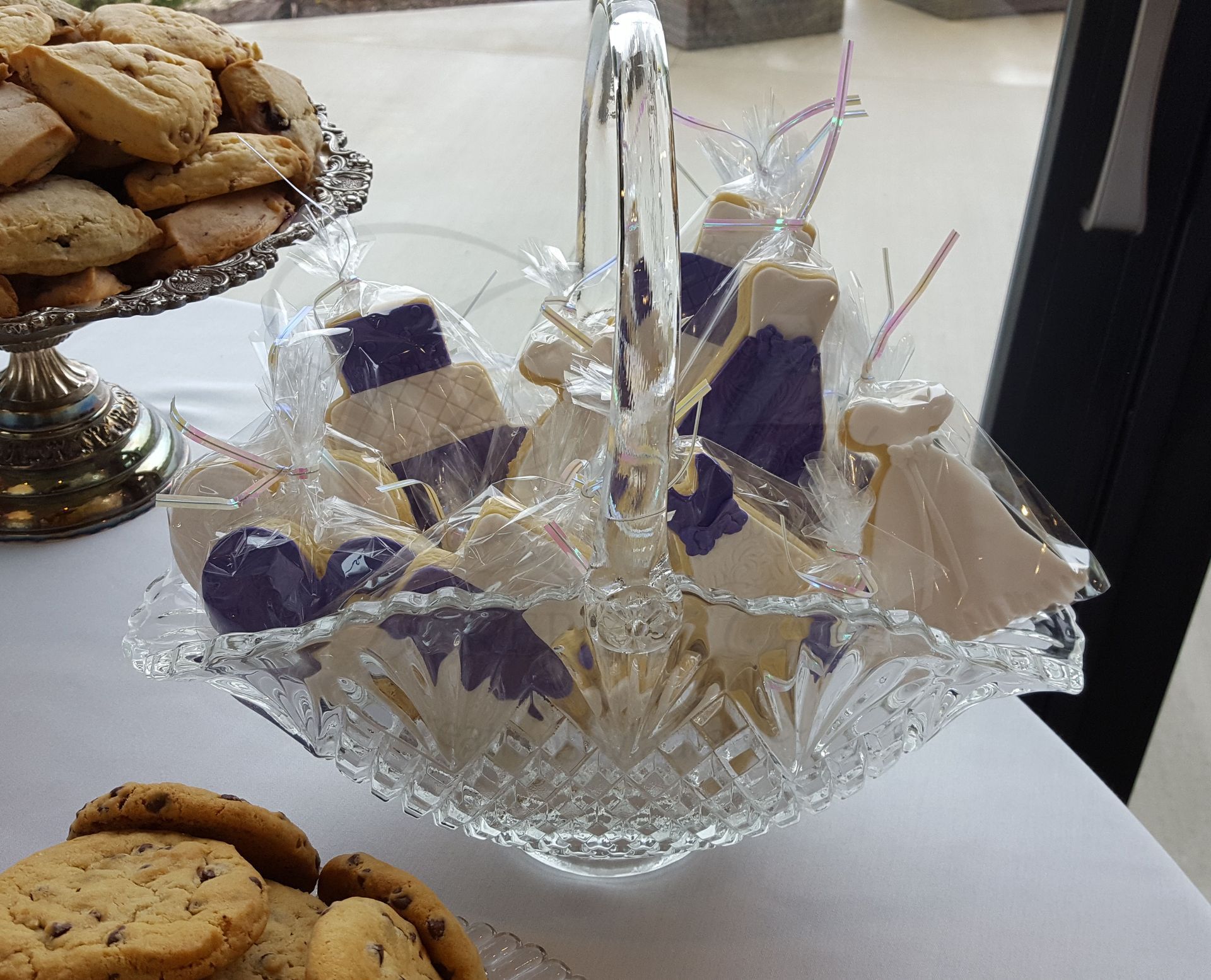 Glass bowl of wrapped purple-and-white treats on a table beside a plate of cookies