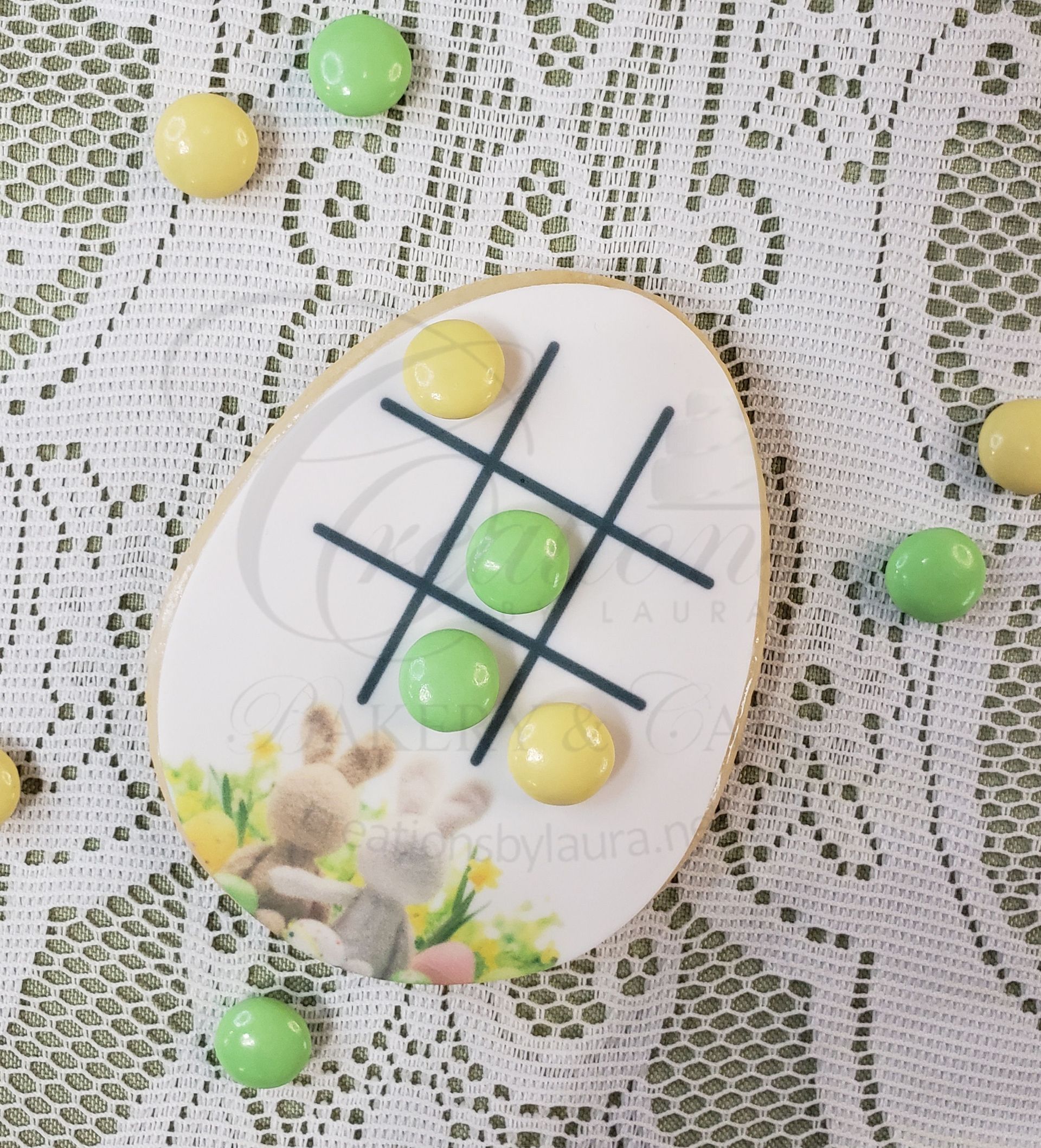 Decorative egg with tic-tac-toe grid and pastel candies on a lace tablecloth.