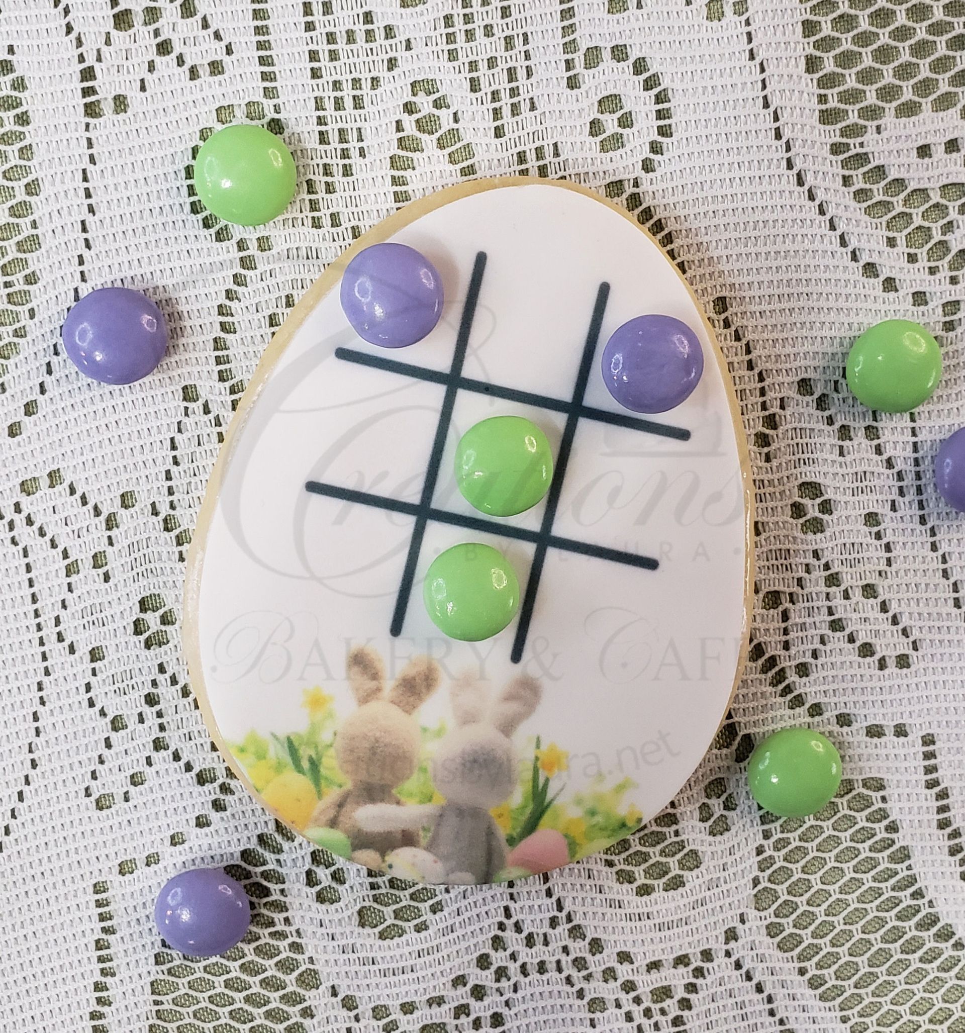Tic-tac-toe on a white egg with purple and green candies on a lace background.