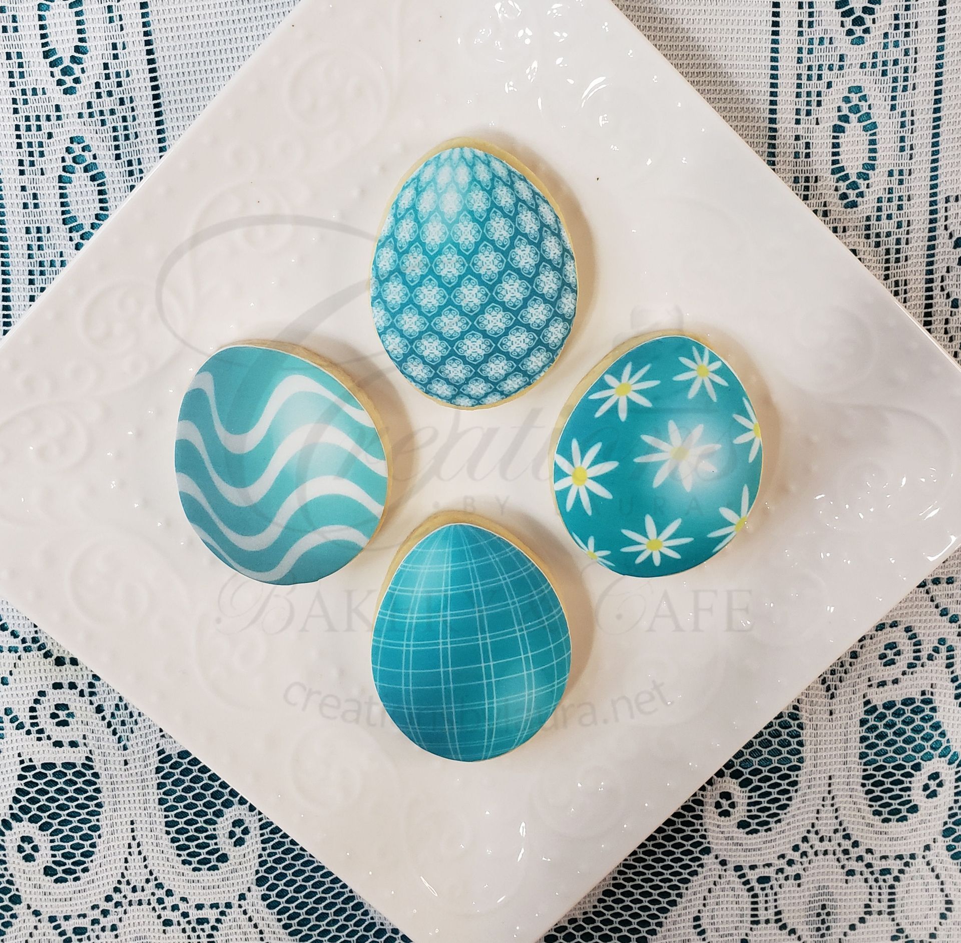 Four decorated blue Easter eggs on a white napkin with a lace tablecloth background.