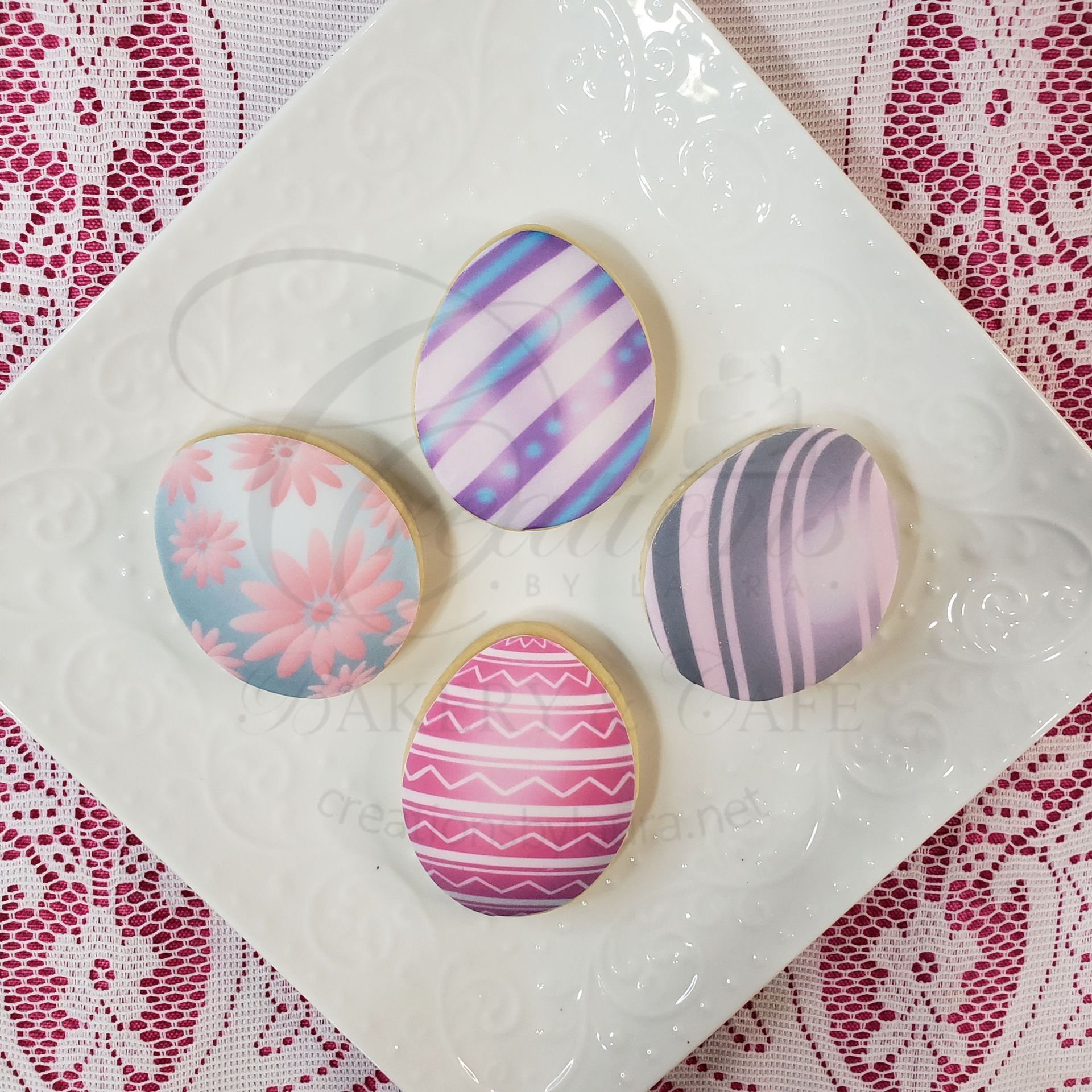 Four pastel decorated Easter eggs on a white plate with a pink patterned tablecloth.