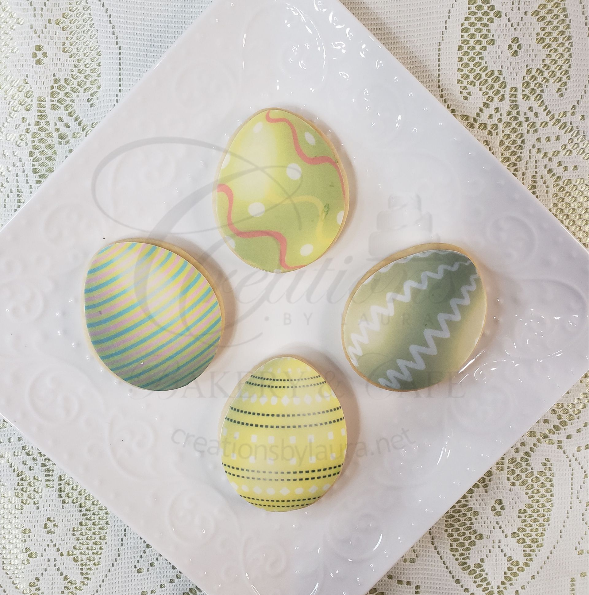 Decorated Easter cookies on a white plate, in pastel yellow, green, and white with striped and zigzag icing.