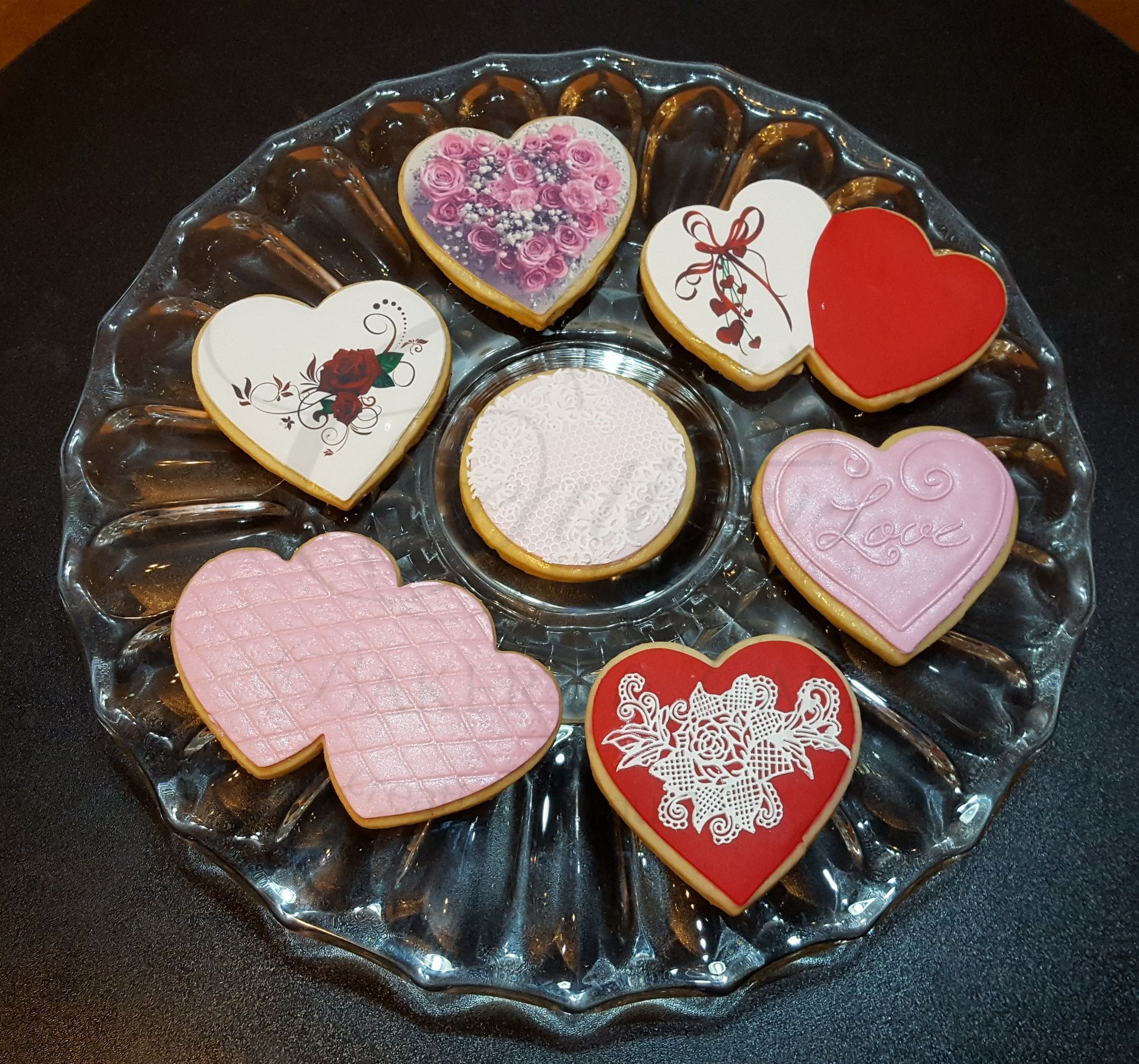 Heart-shaped decorated cookies on a glass plate, in pink, red, white, and gold.