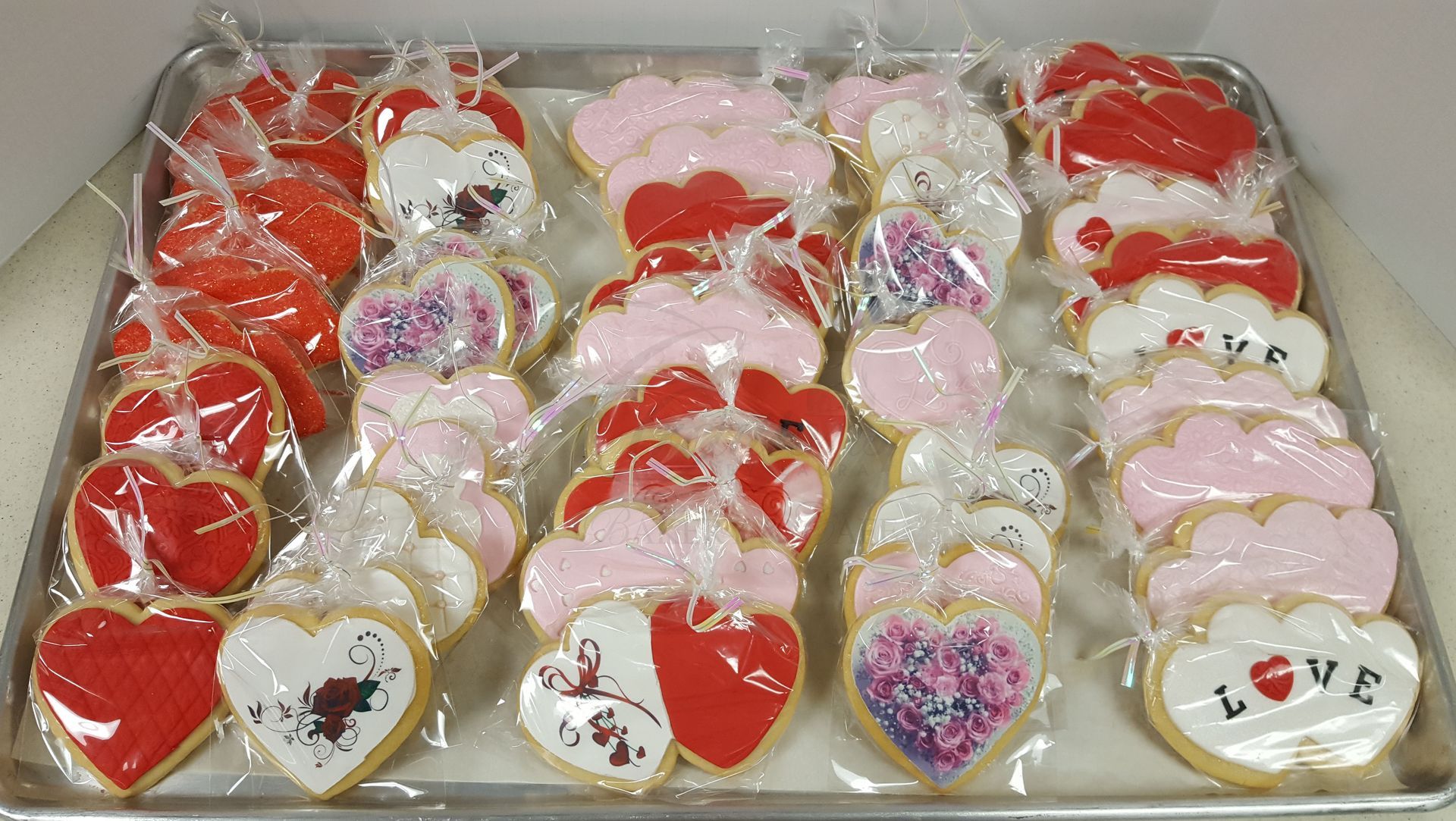 Assorted heart-shaped decorated cookies wrapped in clear plastic, arranged in rows on a tray.