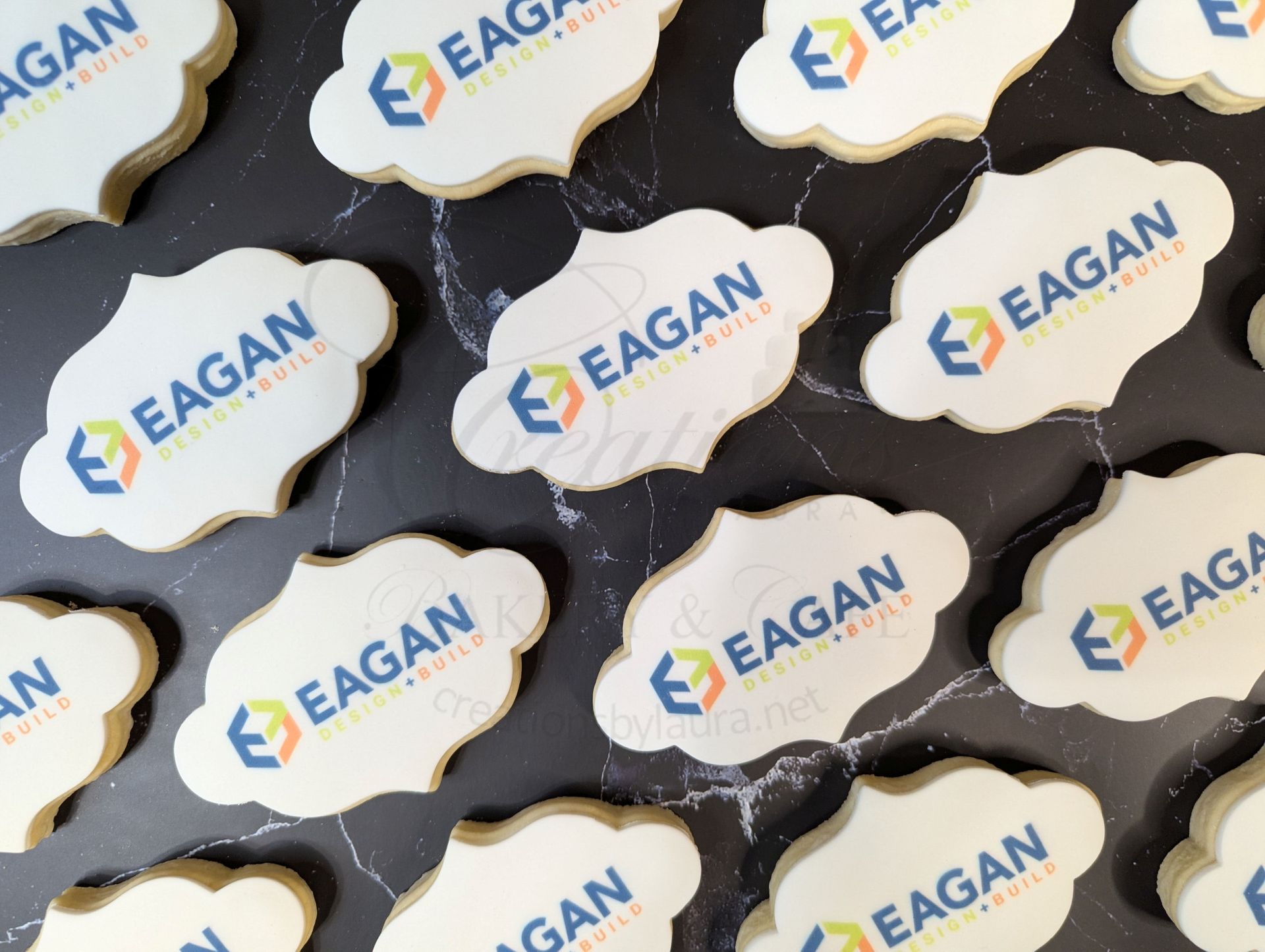 Stack of white EAGAN logo cookies with blue and gold branding on a dark surface.
