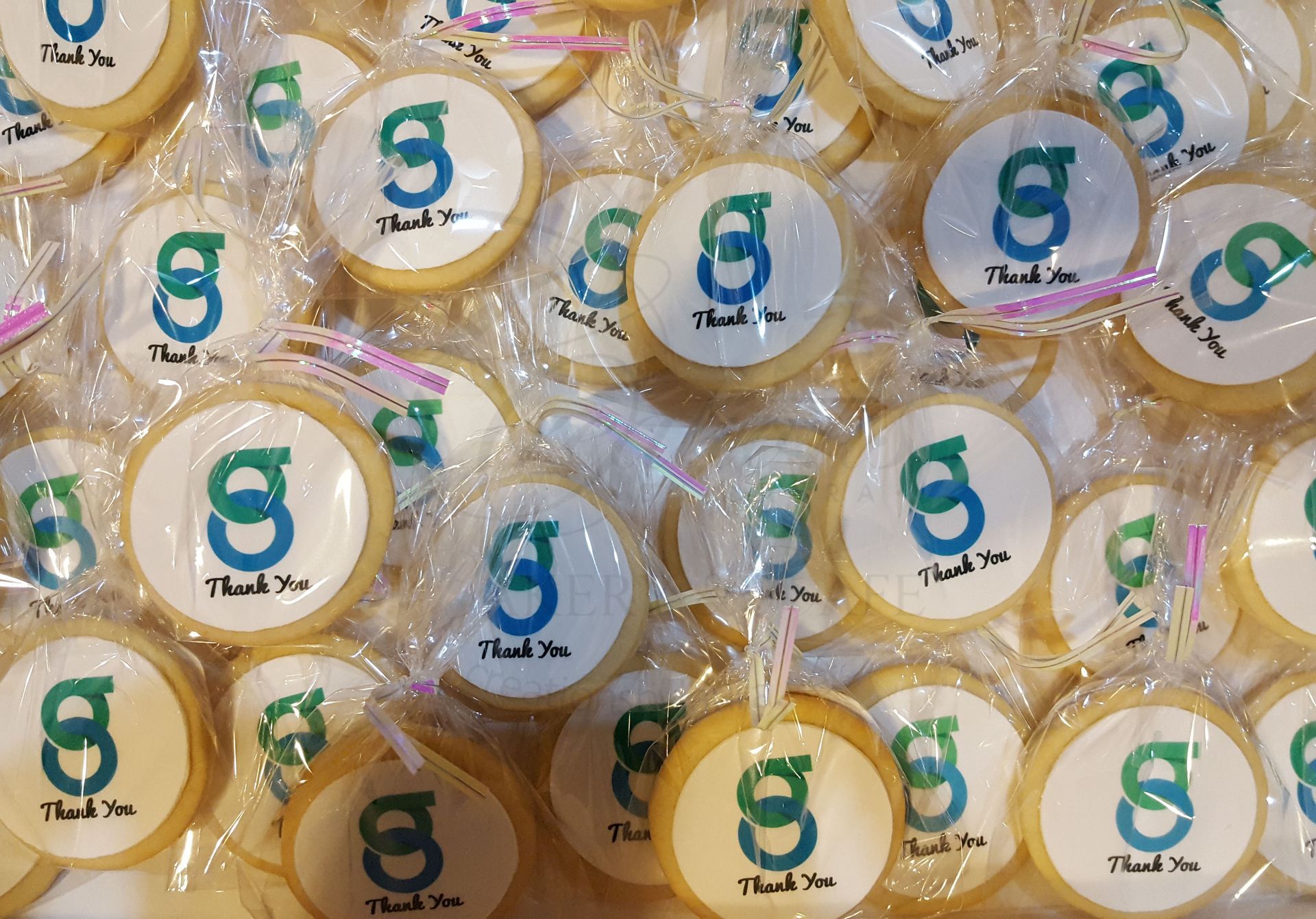 Assorted round gold-and-white gift favors with green and blue S logos, wrapped in clear plastic.