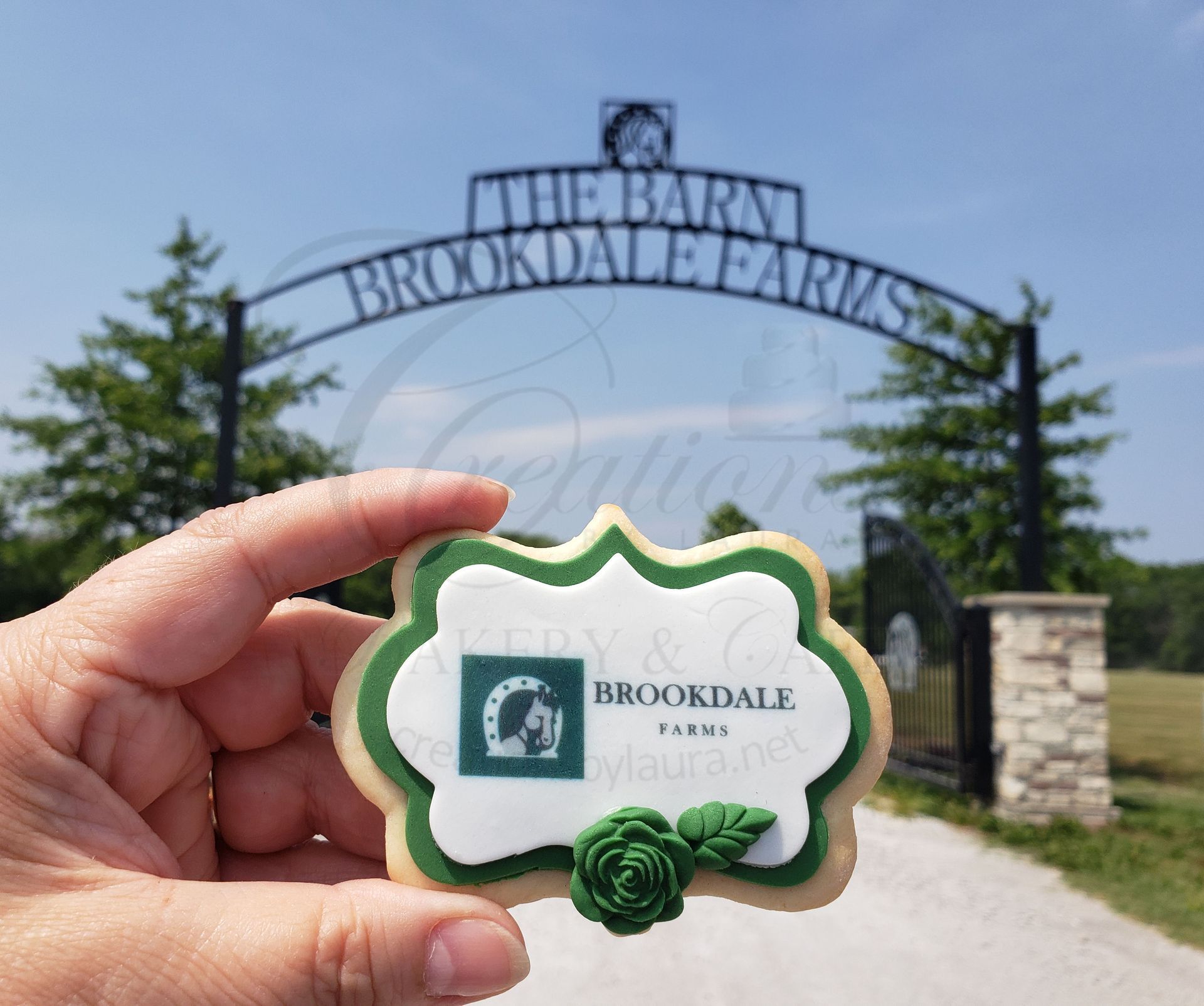 Hand holding a Brookdale Farms ornament in front of the Brookdale Farms entrance sign.