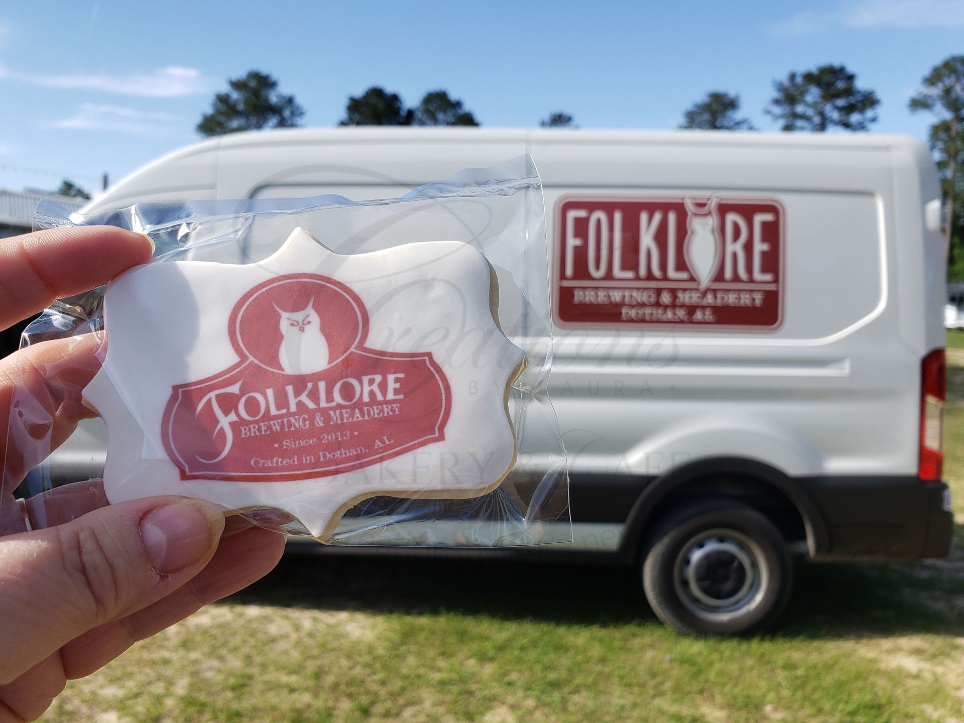 Hand holding a Folklore-branded cookie in front of a white delivery van with a matching sign.