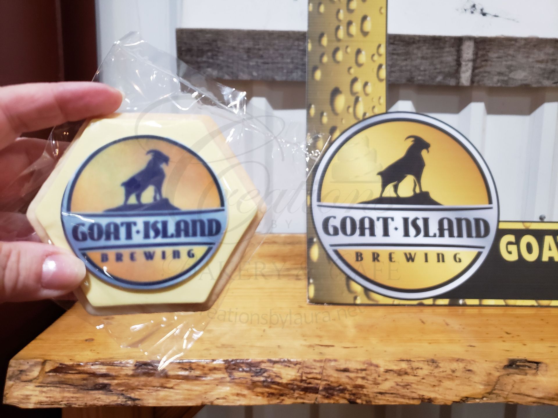 Goat Island Brewing logo sticker held beside a matching coaster on a wooden bar counter.