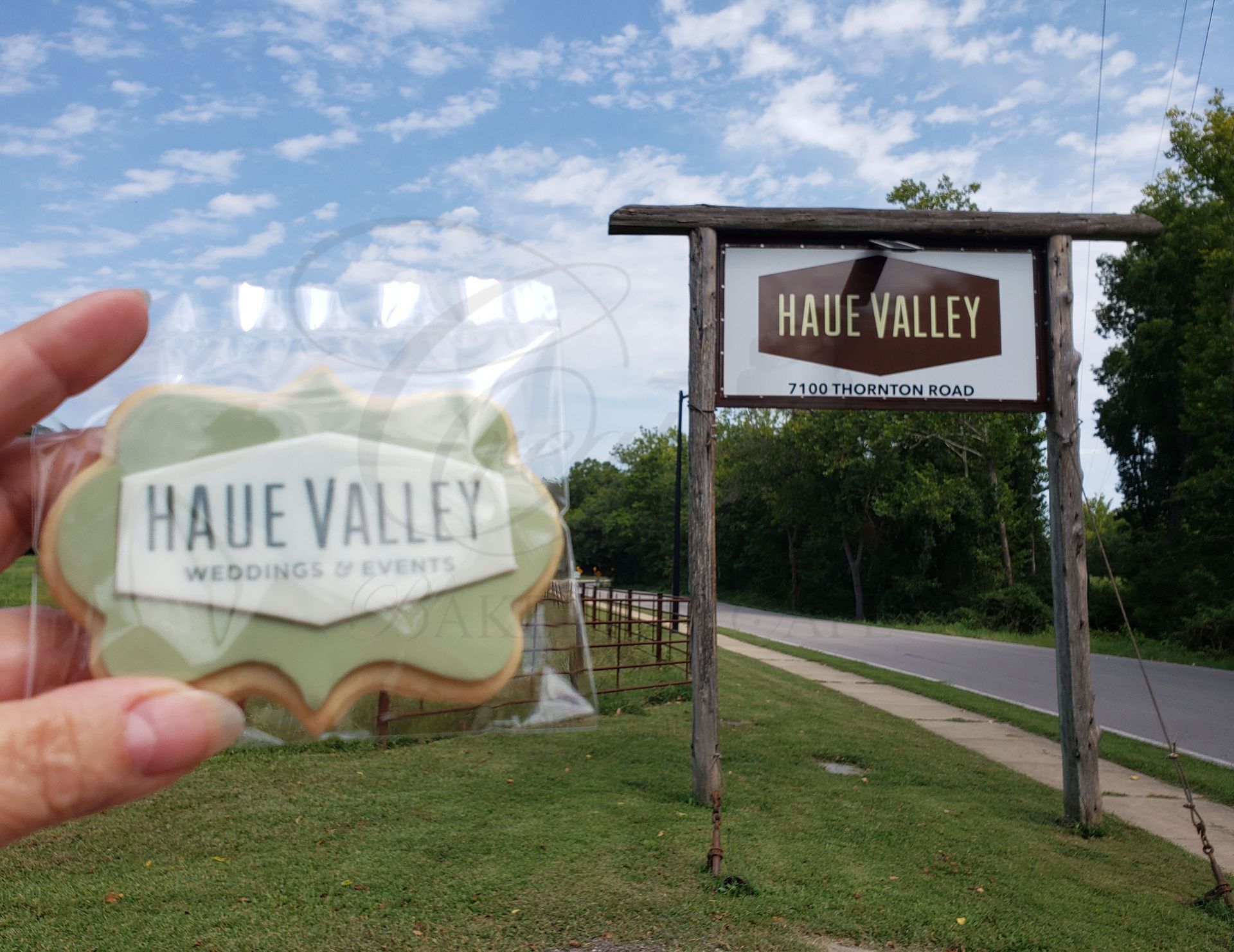 Hand holding a Haue Valley wedding invitation with a matching venue sign by a road.